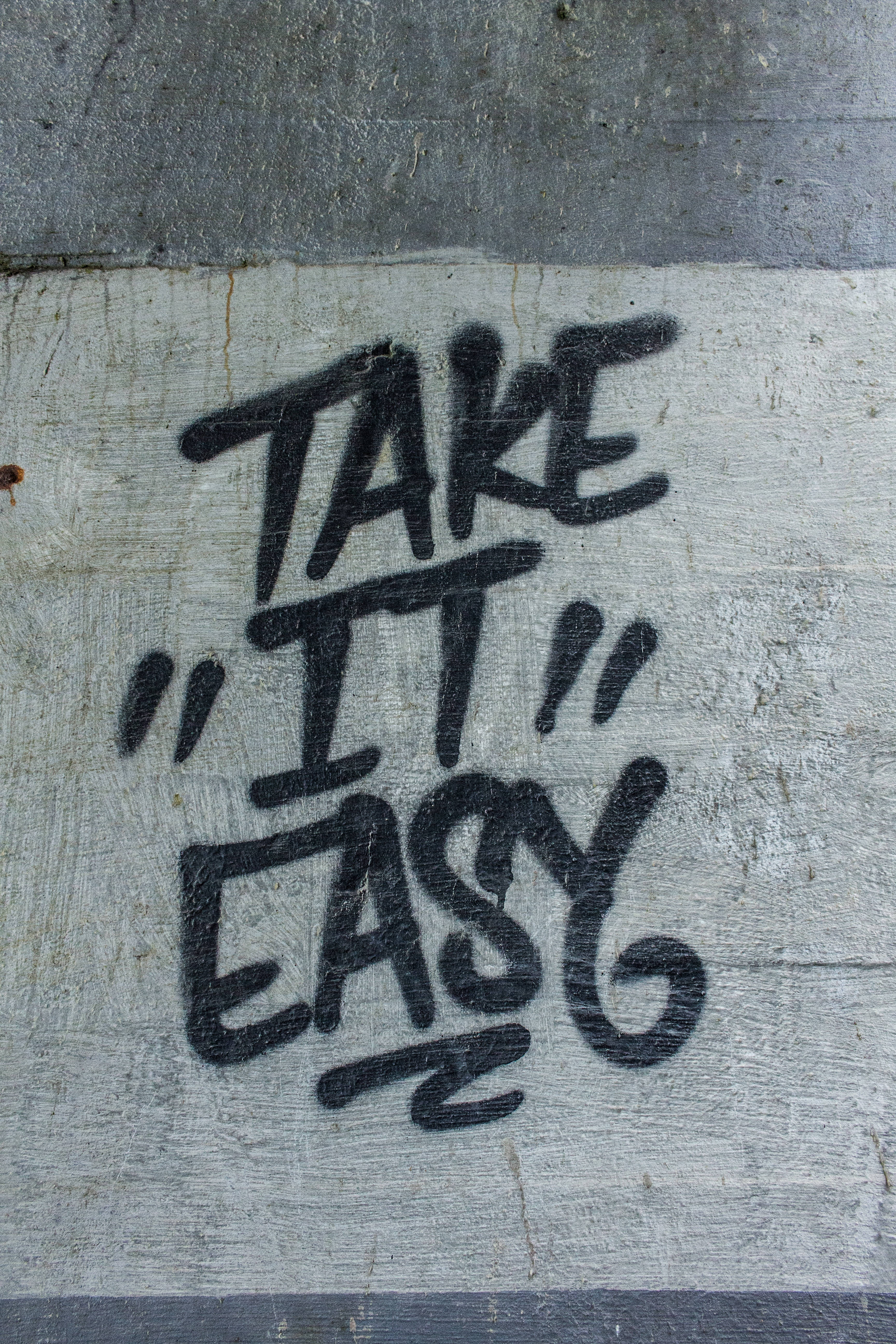 語錄 桌布 壁紙 — 在天橋下風化的混凝土上，粗體黑色塗鴉拼出「TAKE IT EASY」。