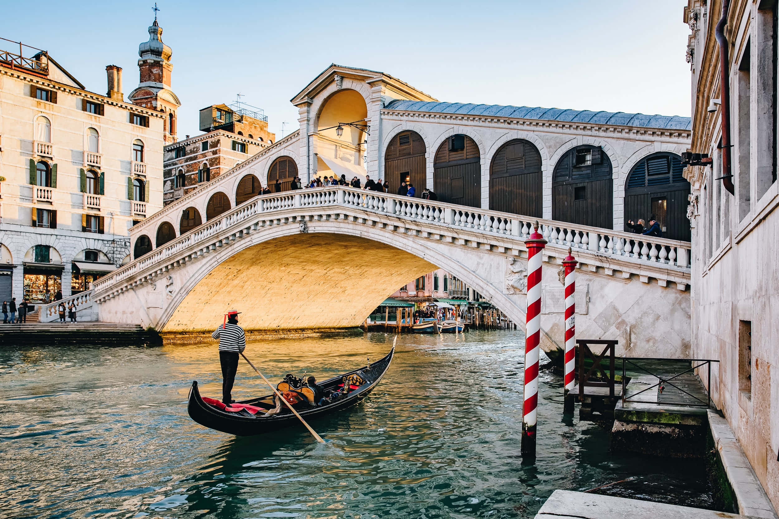 venice 桌布 壁紙 — 在威尼斯黃金時段，一名貢多拉船夫在標誌性的石橋 Ponte di Rialto 下划著黑色貢多拉。