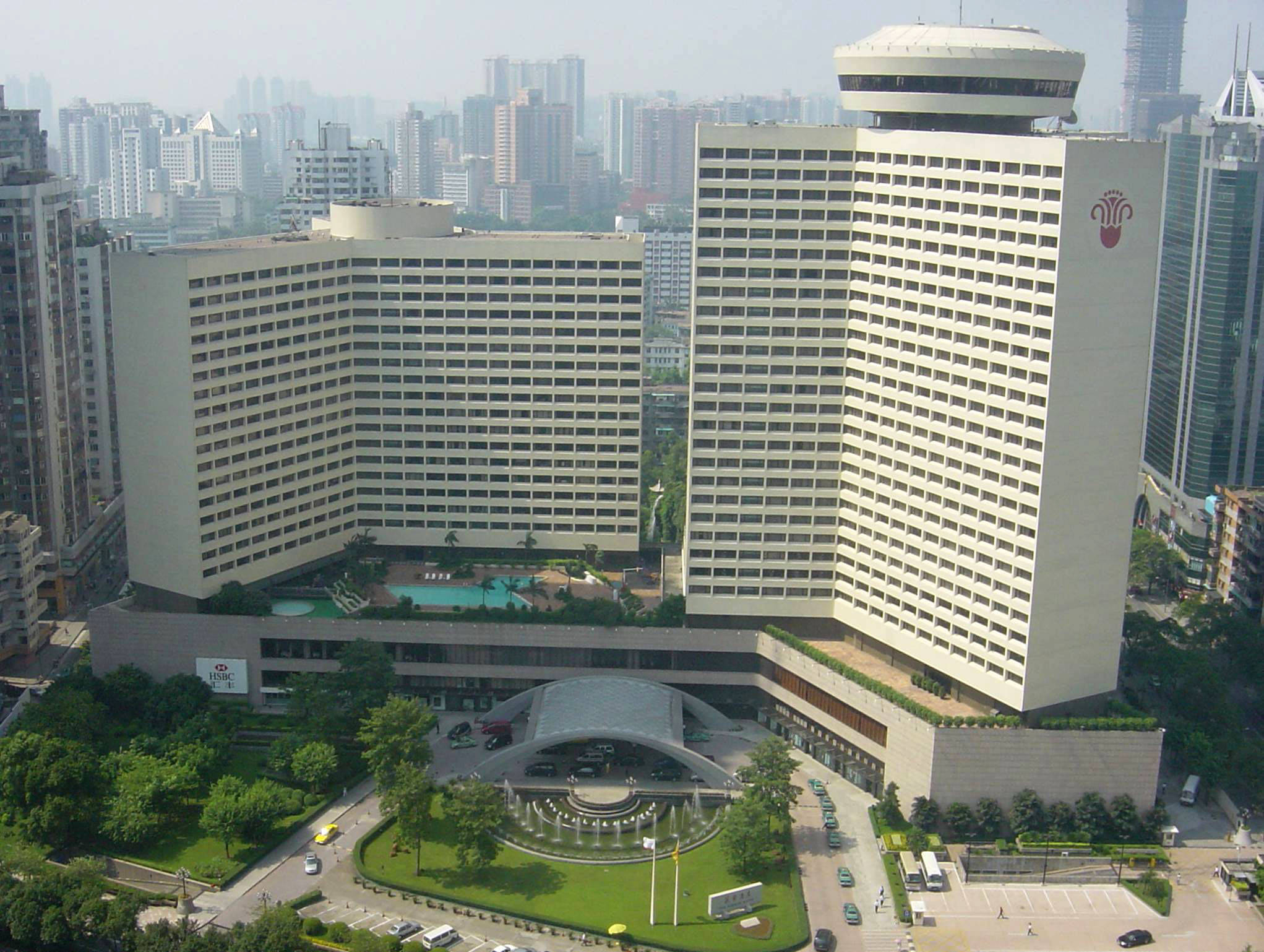 Guangzhou 桌布 壁紙 — 在密集的城市天際線中，一座宏偉的弧形酒店，設有屋頂游泳池和噴泉，周圍環繞著茂密的綠植的鳥瞰圖。