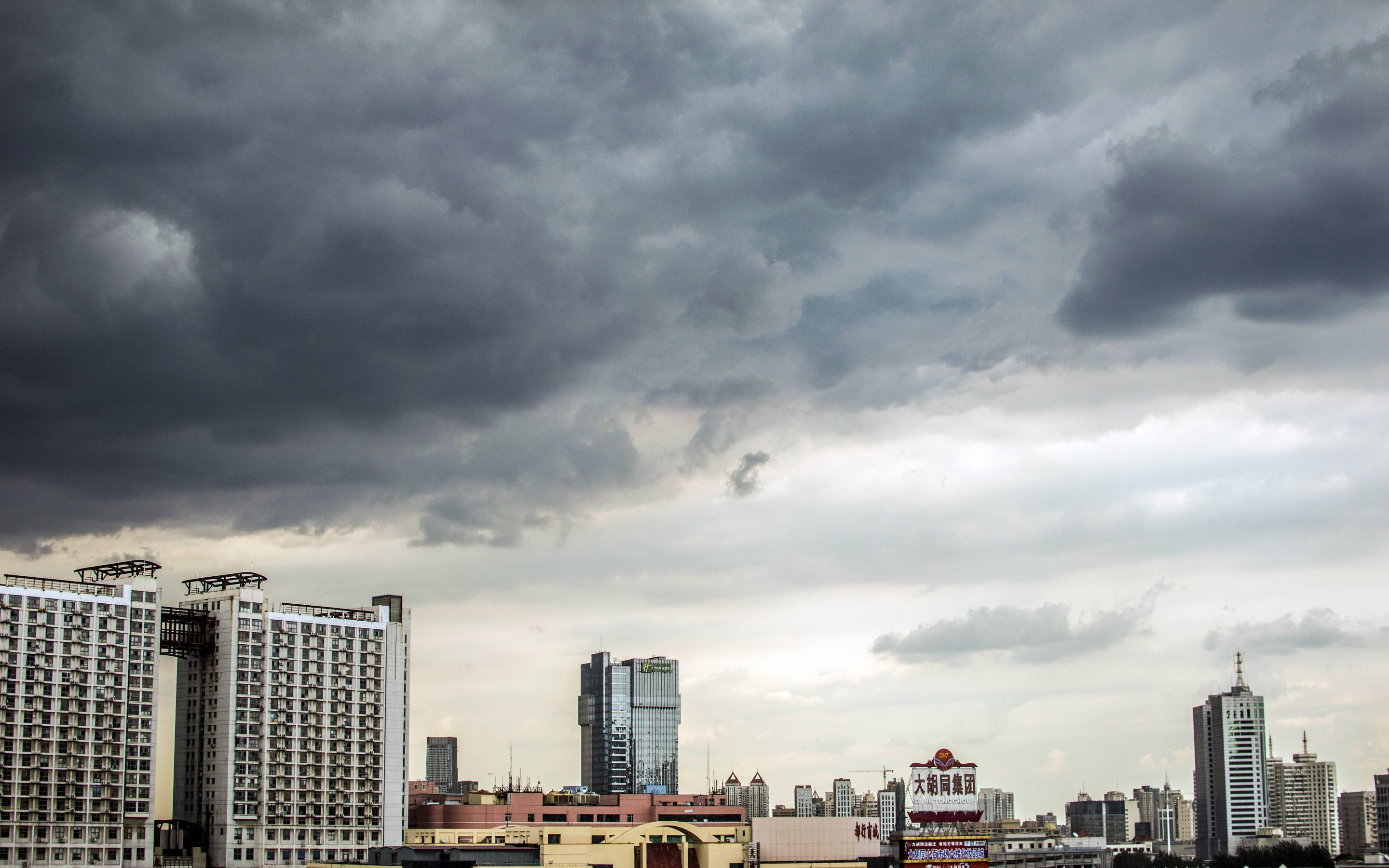 Tianjin 桌布 壁紙 — 在密雲密佈的天空下，現代與舊式建築上方籠罩著黑暗的暴風雲，構成戲劇性的城市天際線。