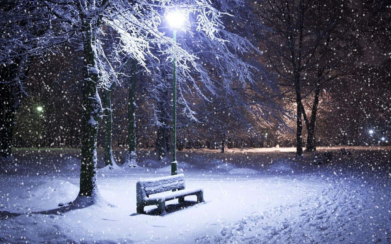 Winter Night Desktop 桌布 壁紙 — 在寧靜的冬夜公園裡，一張孤獨的積雪長椅在街燈下閃耀，雪花輕輕飄落。