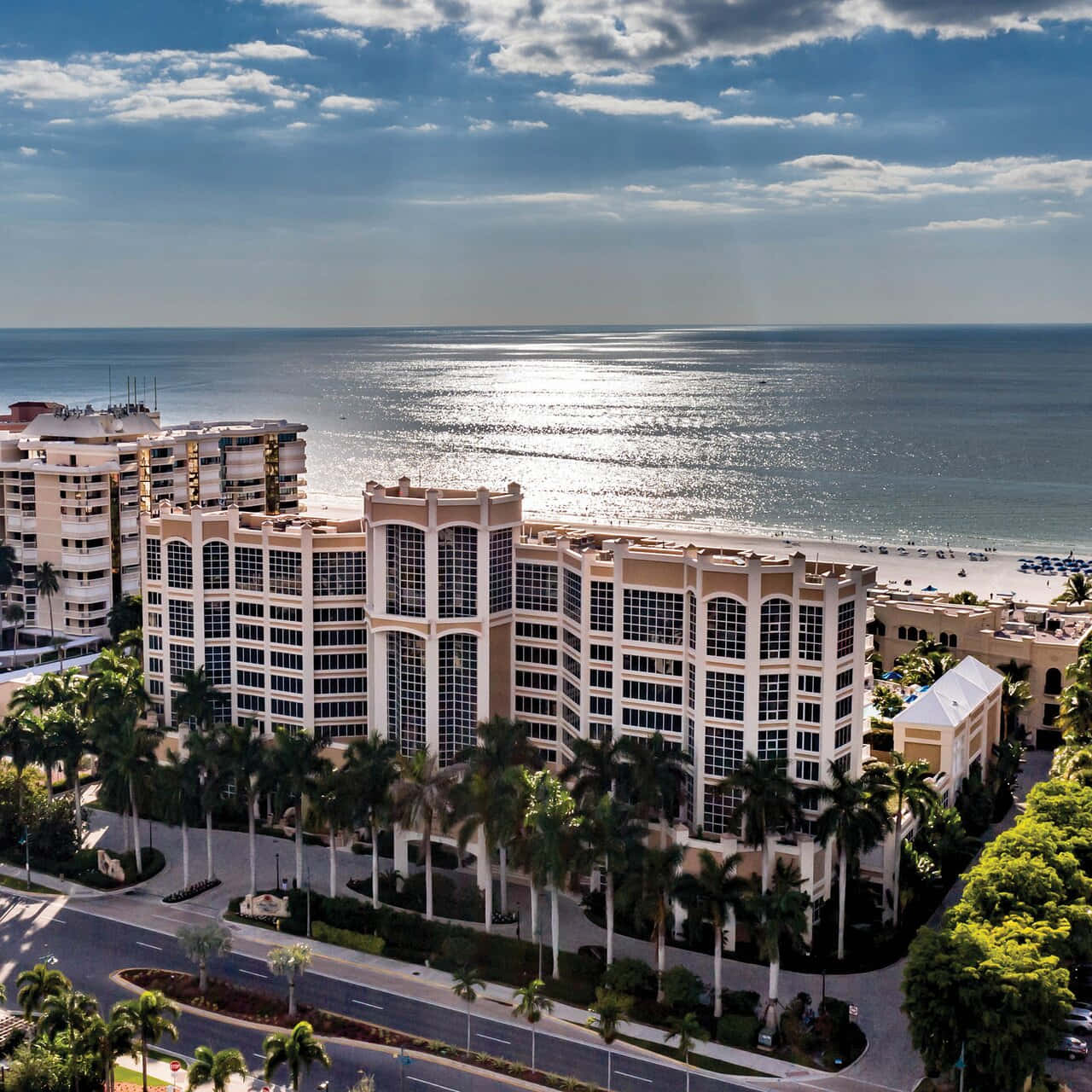 Marco Island 桌布 壁紙 — 在局部多雲的天空下，一個宏偉的海濱酒店綜合體的航拍視圖，有棕櫚樹和閃閃發光的海洋。