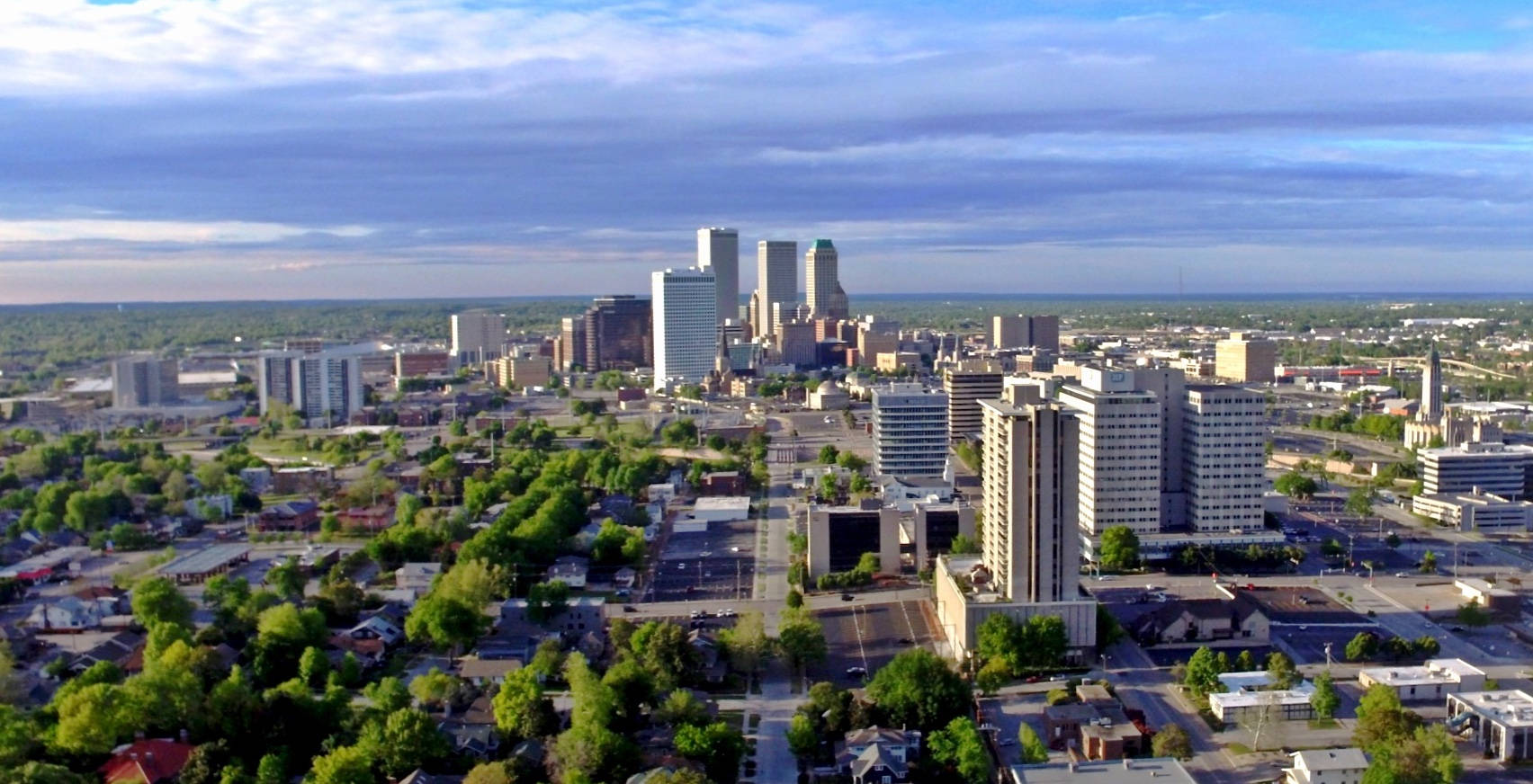 Oklahoma 桌布 壁紙 — 在局部多雲的天空下，一個廣闊城市景觀的航拍圖，有現代摩天大樓和茂密的綠色樹木。
