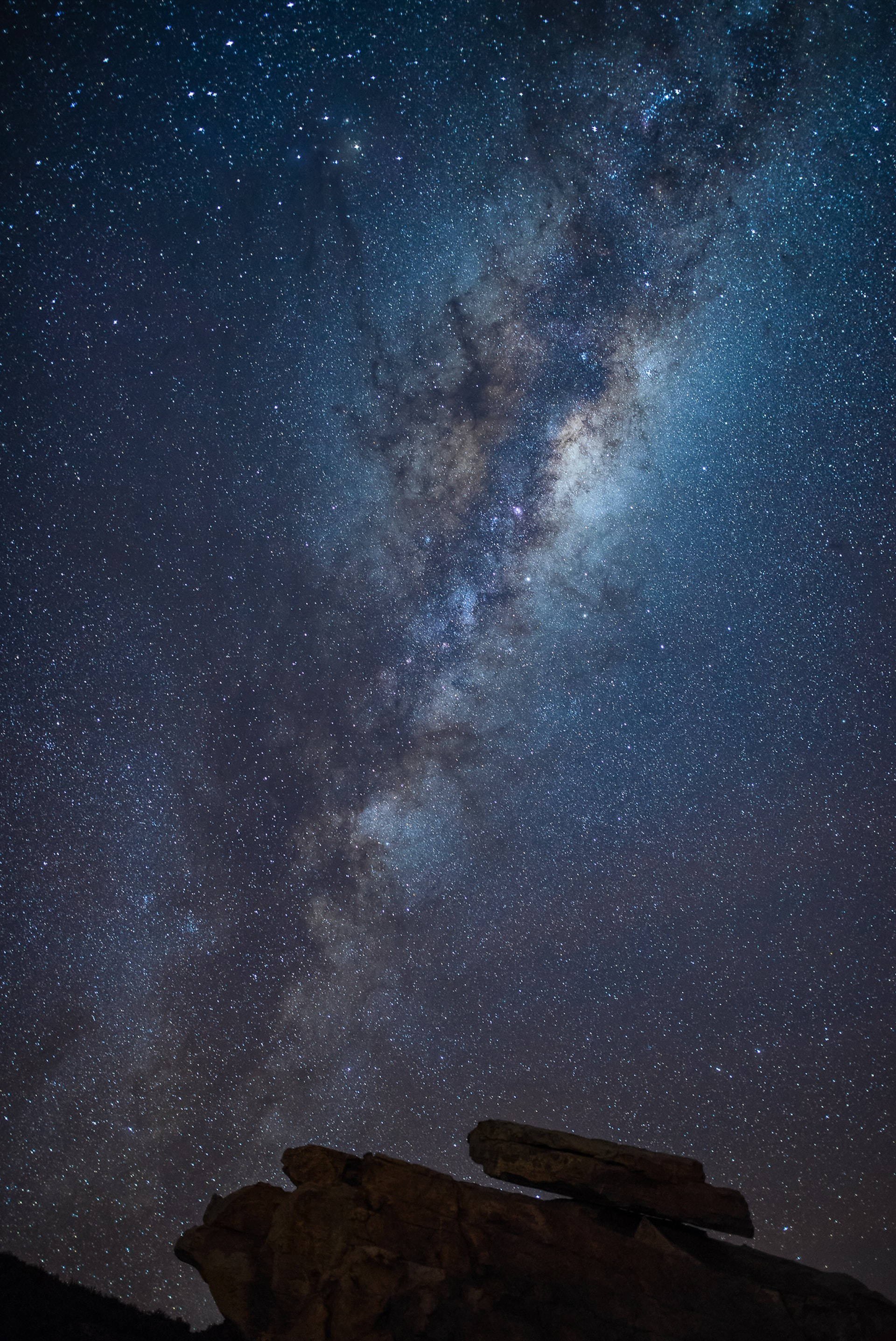 夜空 桌布 壁紙 — 在崎嶇的黑色岩石上方，銀河系橫跨繁星點點的夜空，景色令人嘆為觀止。