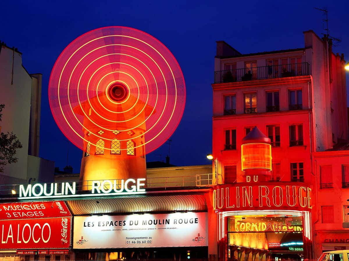 moulin rouge 桌布 壁紙 — 在巴黎標誌性的紅磨坊劇院上方，一個充滿活力的紅色霓虹摩天輪在深藍色的夜空中閃耀。