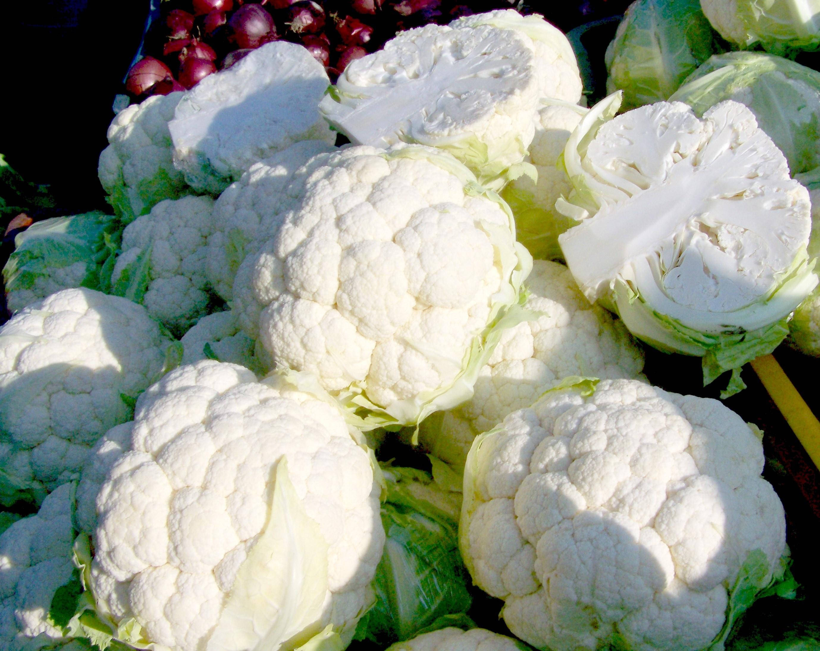 Vegetables 桌布 壁紙 — 在市場攤位上，陽光下高高堆起的帶有綠色葉子的亮白色花椰菜頭。