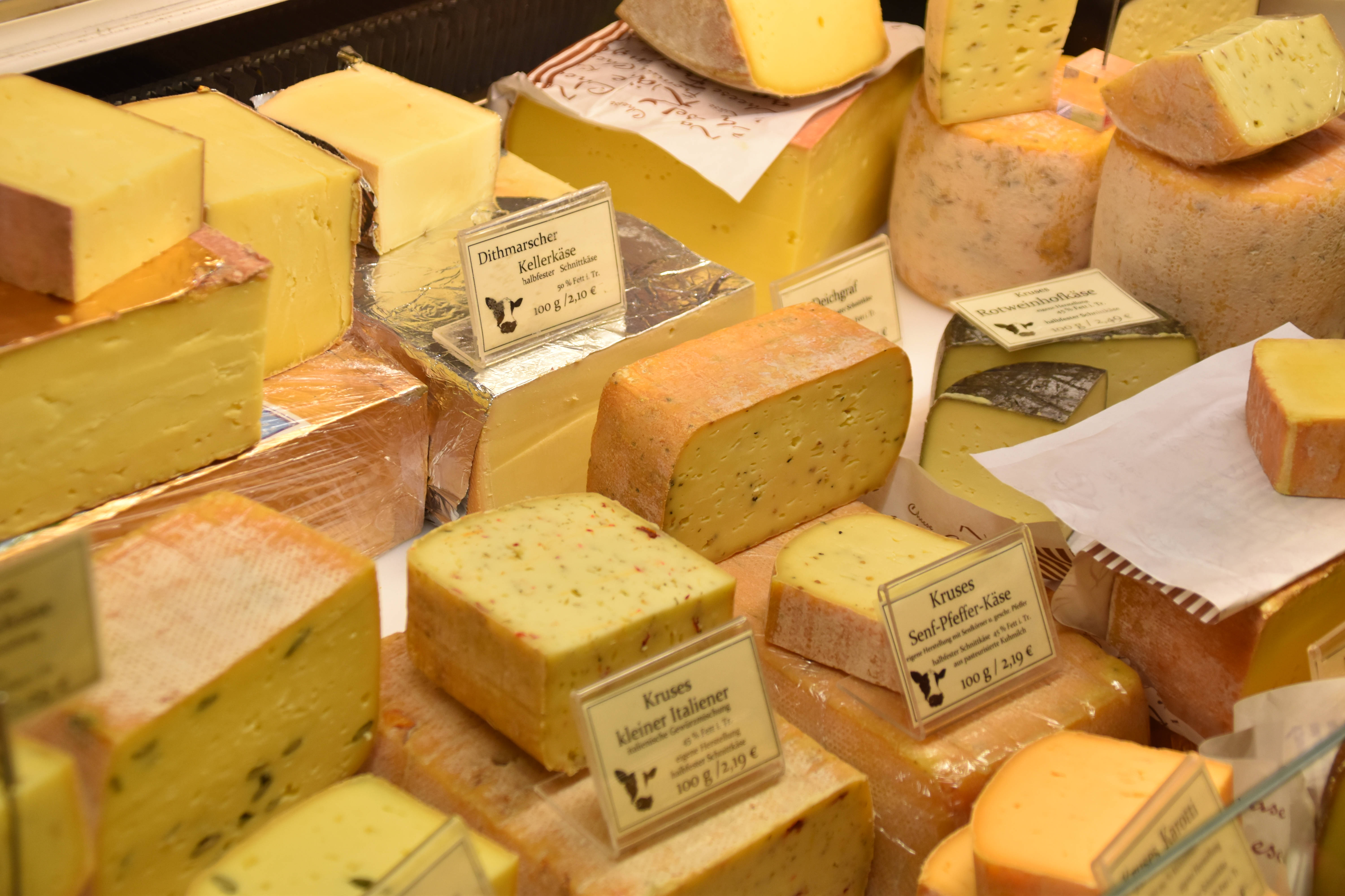 Cheese 桌布 壁紙 — 在市場攤位上展示各種手工起司，附有標籤和不同質感，色彩繽紛。