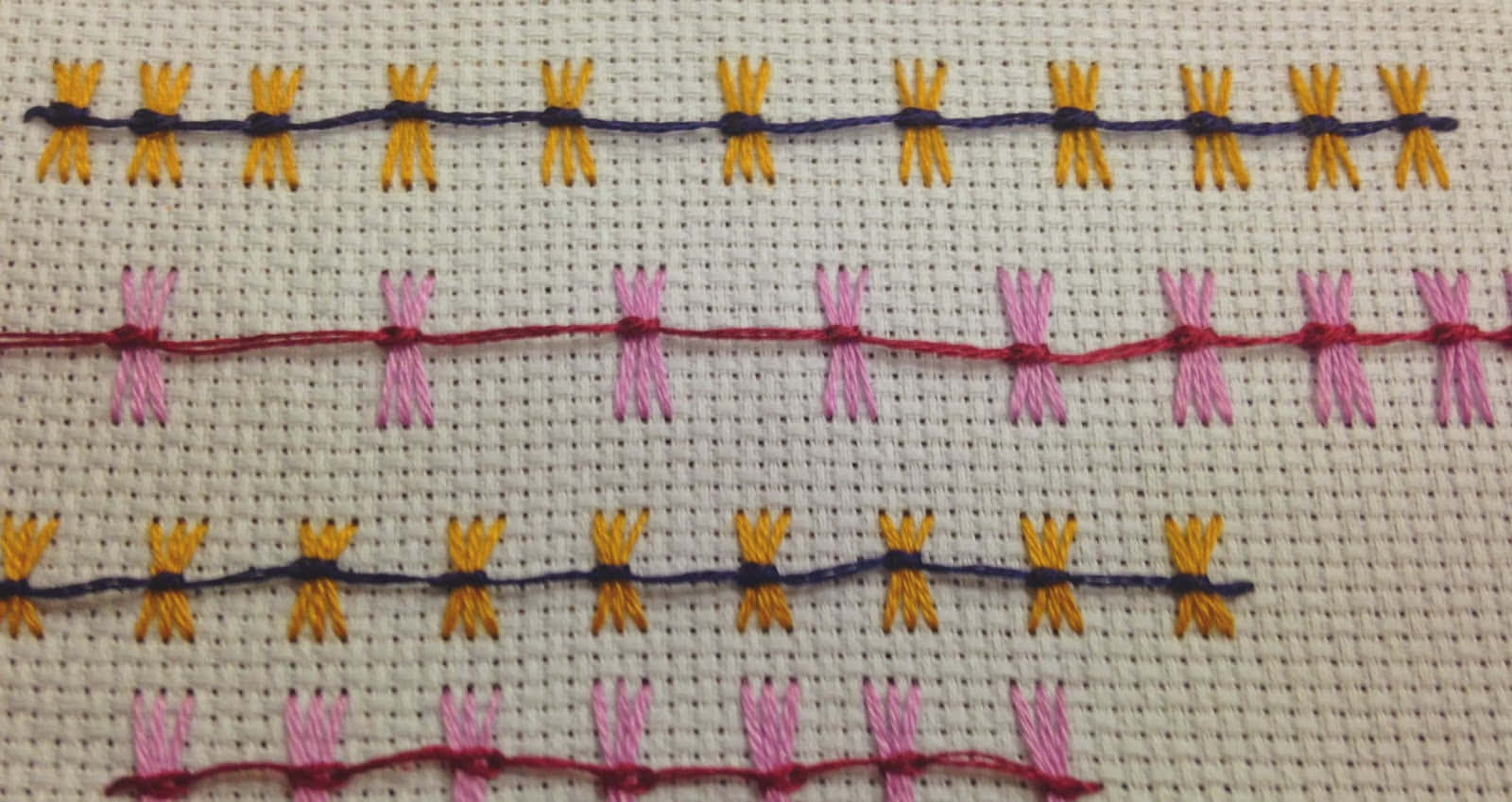 Butterfly Stitch 桌布 壁紙 — 在帶有紋理的白色布料上，排列著黃色、粉紅色和紫色的彩色刺繡蜻蜓。