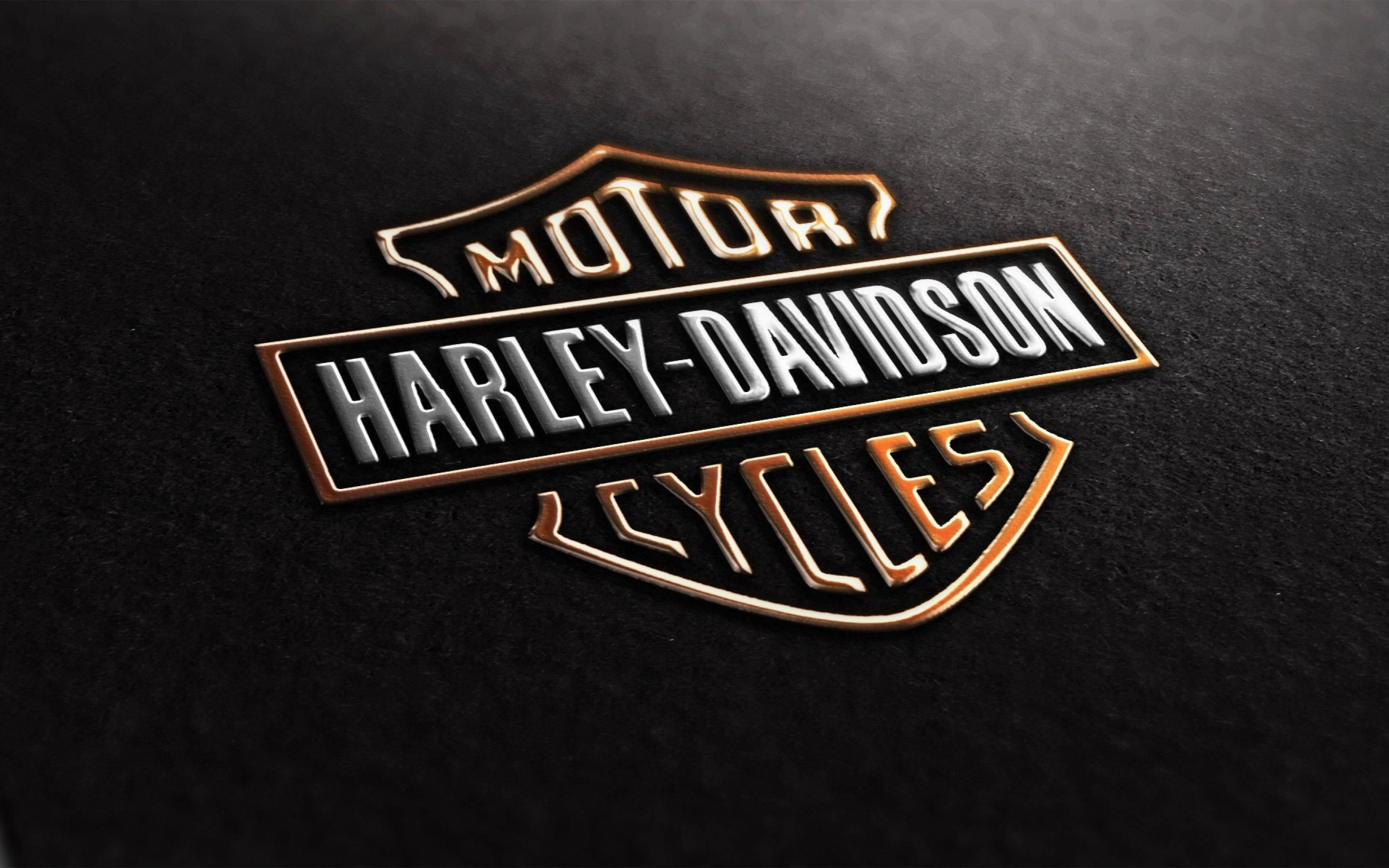 Harley 桌布 壁紙 — 在帶有紋理的黑色表面上，標誌性的哈雷戴維森標誌以金屬金色和銀色特寫。