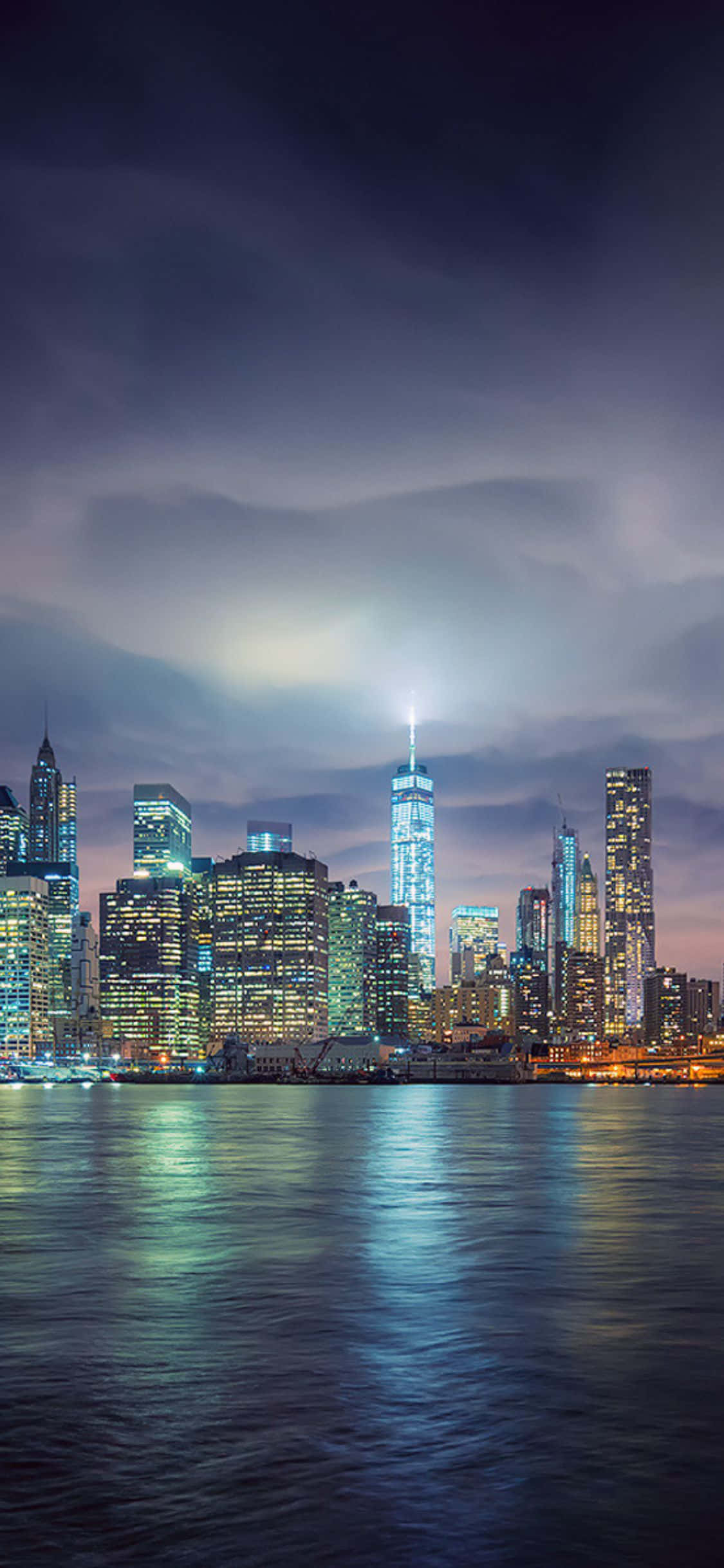 iPhone X New York 桌布 壁紙 — 在憂鬱的暮色天空下，紐約天際線倒映在平靜水面上的充滿活力的夜景。