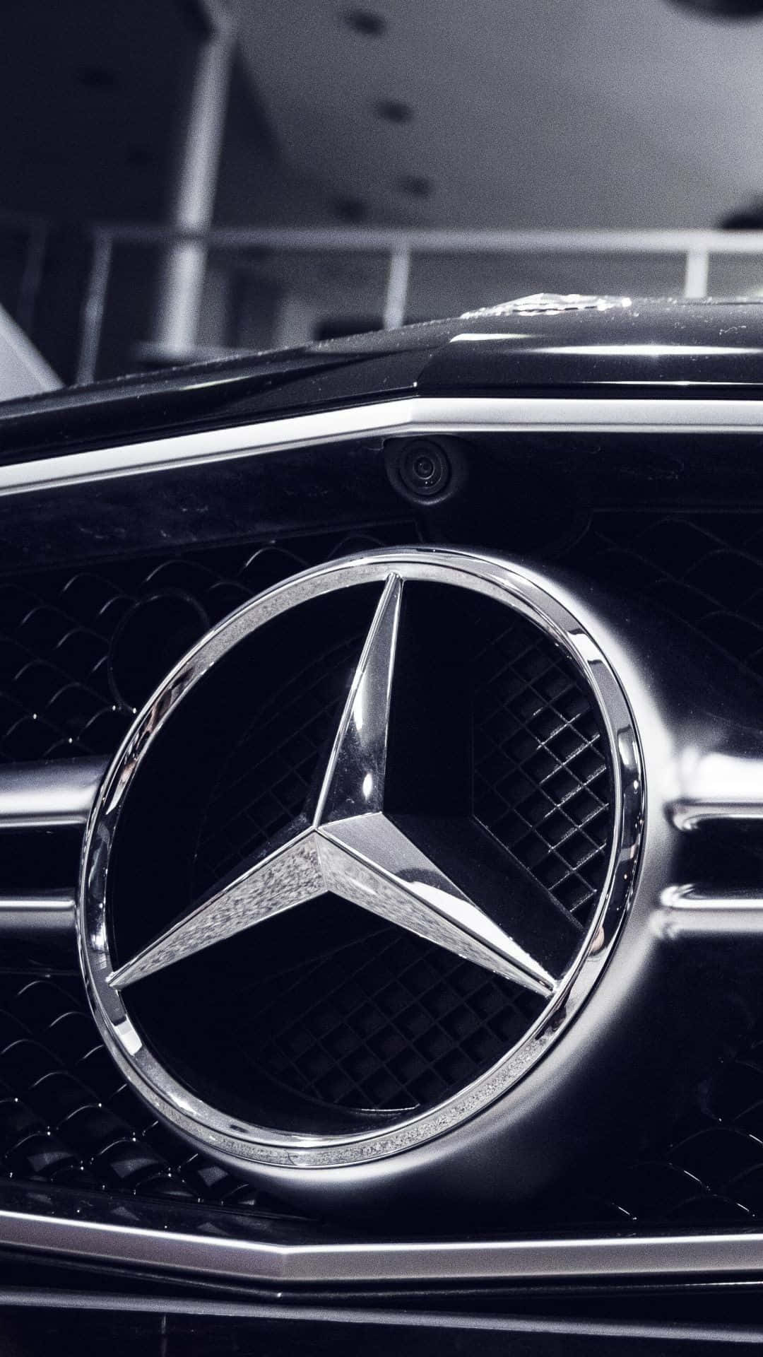 Mercedes 桌布 壁紙 — 在戲劇性工作室燈光下，黑色汽車格柵上閃閃發光的賓士星形標誌特寫。