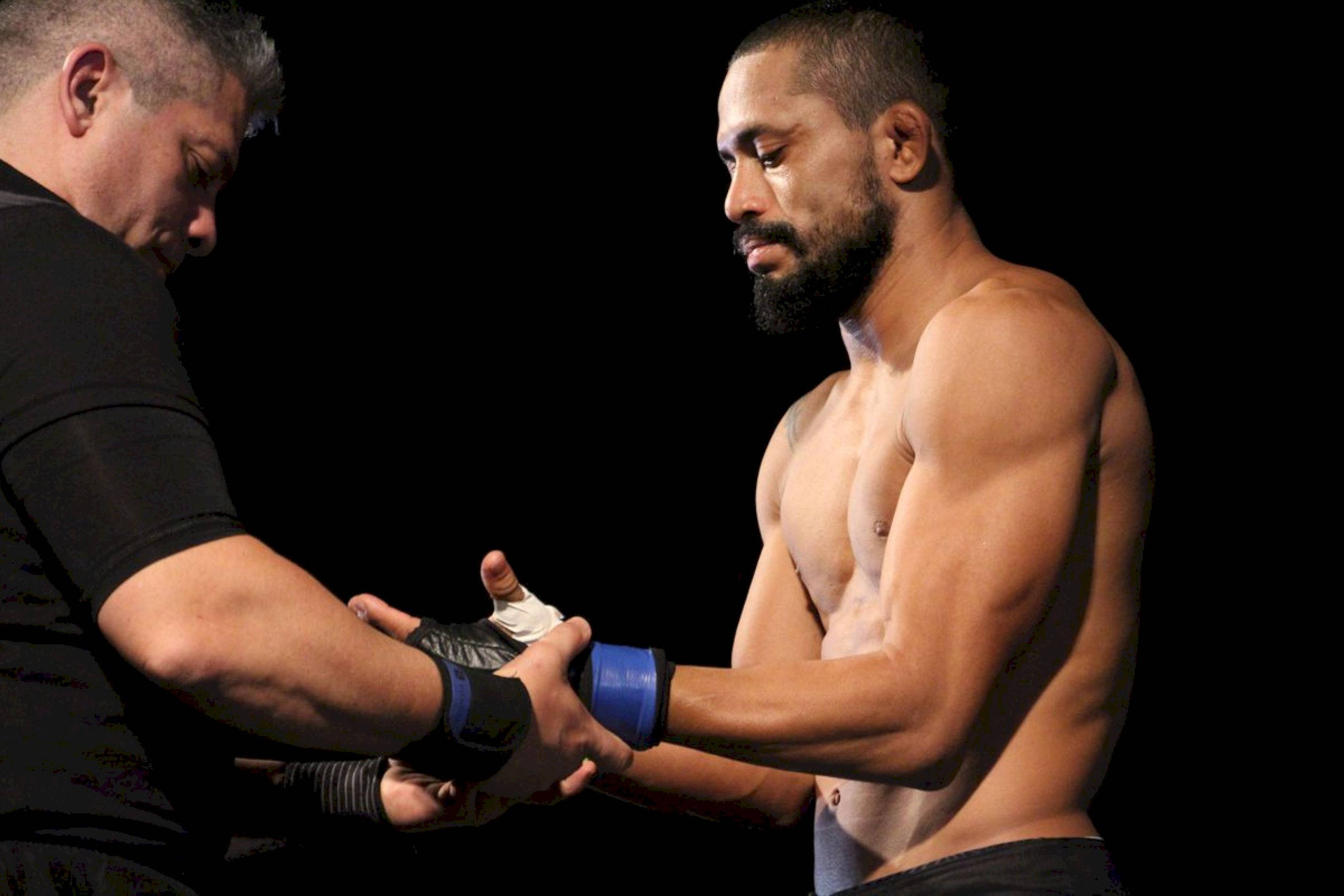 UFC 桌布 壁紙 — 在戲劇性燈光下，一位肌肉發達的拳擊手在純黑背景前接受教練纏手帶。