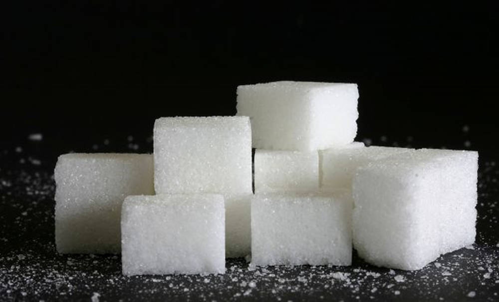 Sugar 桌布 壁紙 — 在戲劇性燈光下，堆疊的白方糖和散落在深色表面上的糖粒。