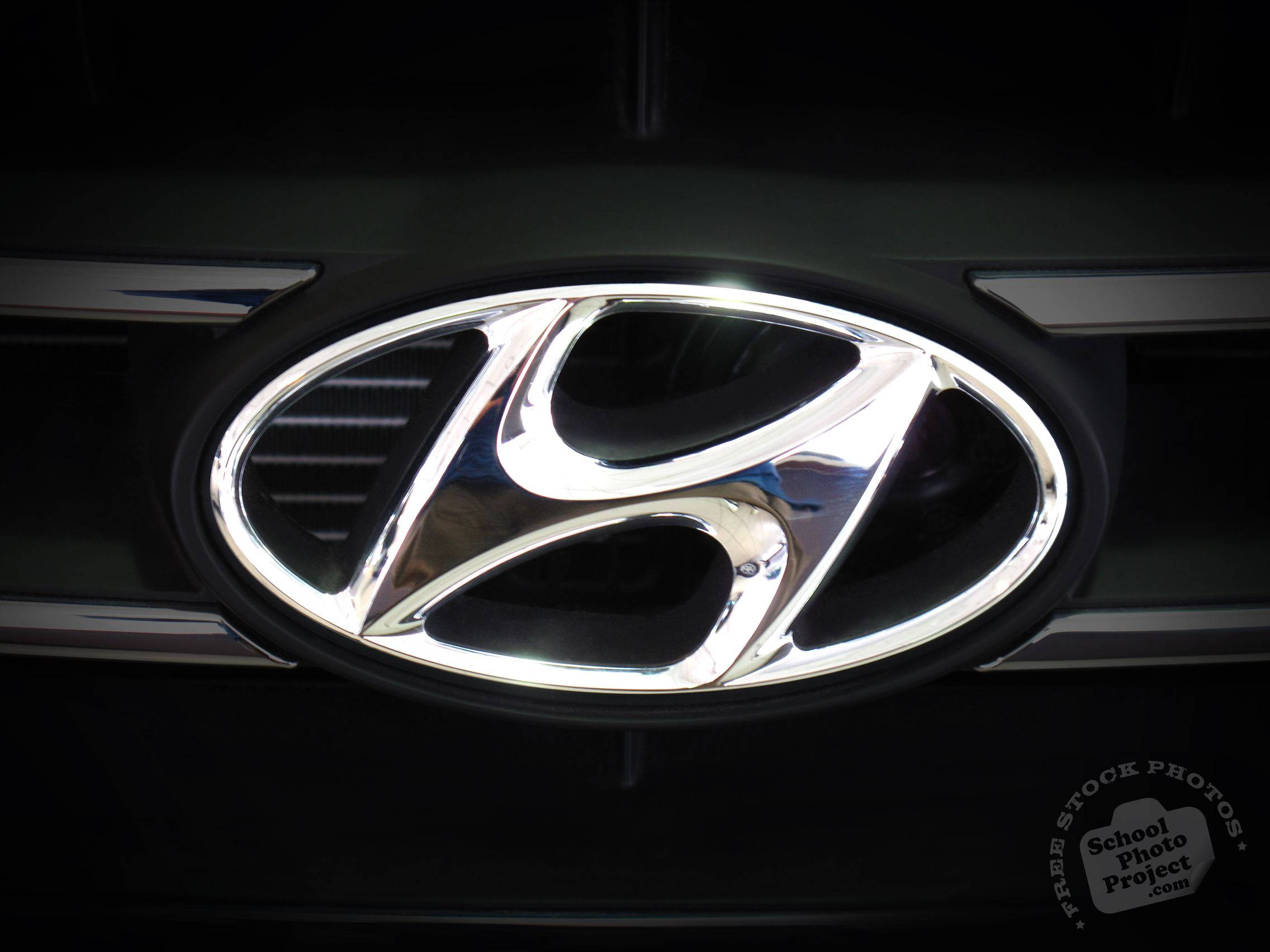 Hyundai 桌布 壁紙 — 在戲劇性燈光下，深色汽車格柵上閃亮鍍鉻現代標誌的特寫。