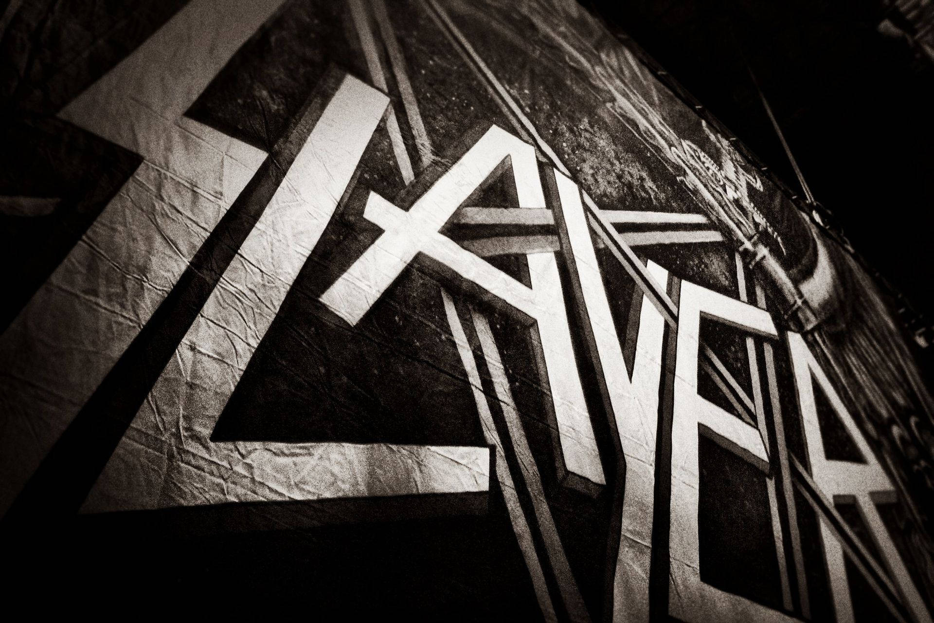 Slayer 桌布 壁紙 — 在戲劇性的低角度燈光下，皺巴巴的黑色表面上拼寫著 'LAYER' 的粗體白色塗鴉字母。