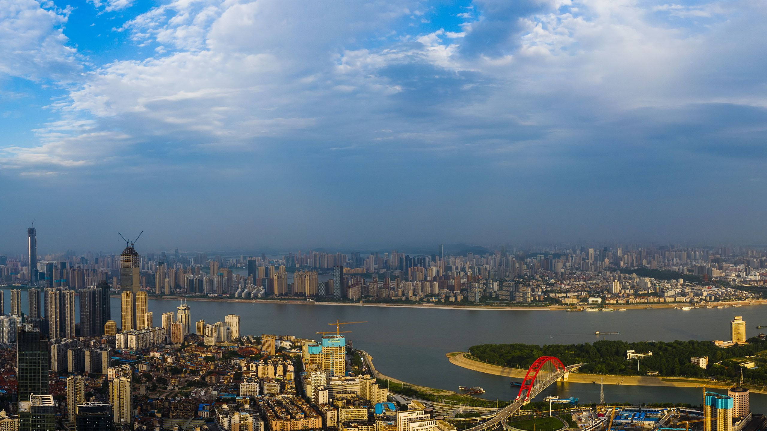 Wuhan 桌布 壁紙 — 在戲劇性的多雲天空下，一條寬闊河流劃分的廣闊城市景觀的鳥瞰圖。