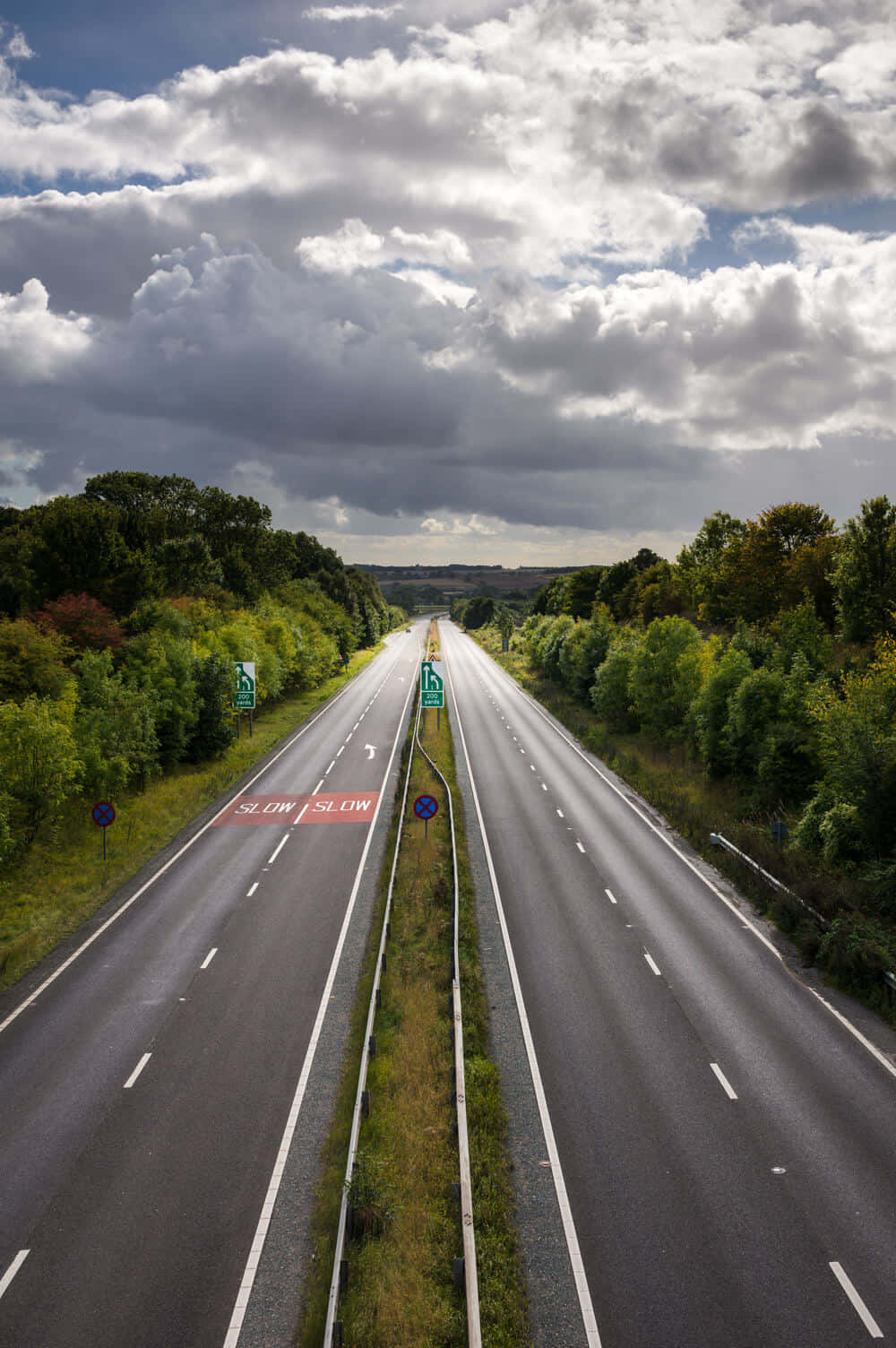Highways 桌布 壁紙 — 在戲劇性的多雲天空下，一條長直高速公路兩旁綠樹成蔭的鳥瞰圖。