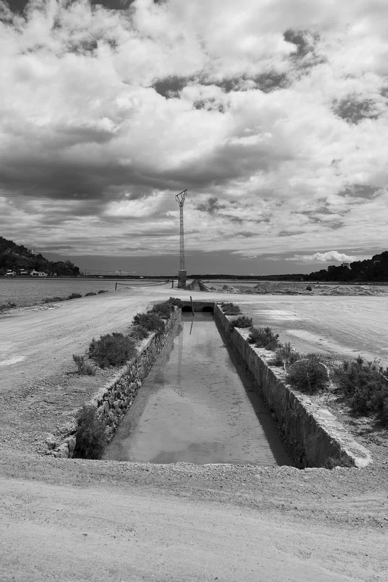 water 壁紙 — 在戲劇性的多雲天空下，一條長長的石砌運河延伸至遠處塔樓的單色景觀。
