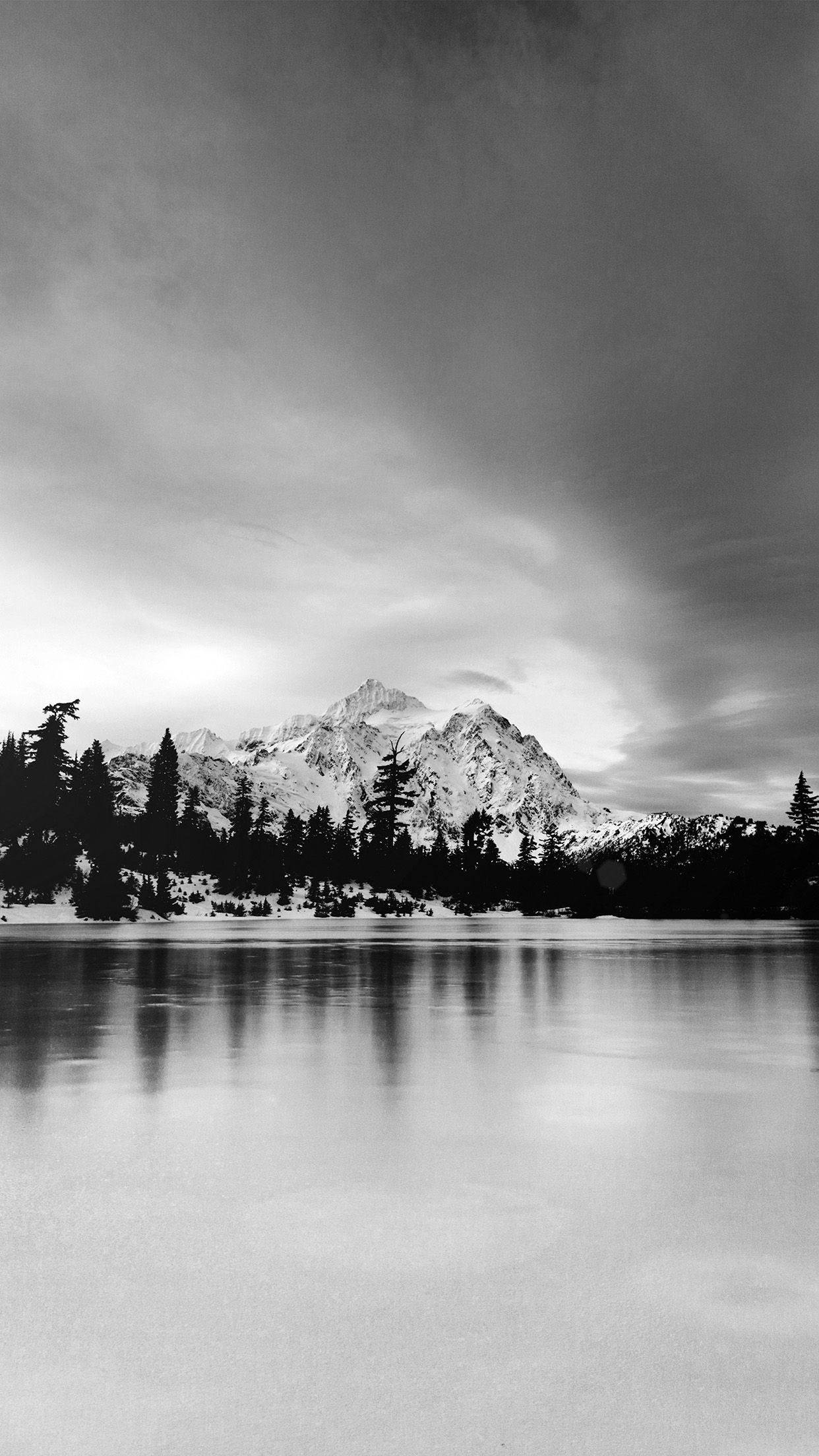 Black And White iPhone 桌布 壁紙 — 在戲劇性的多雲天空下，單色山峰倒映在平靜的湖面上。