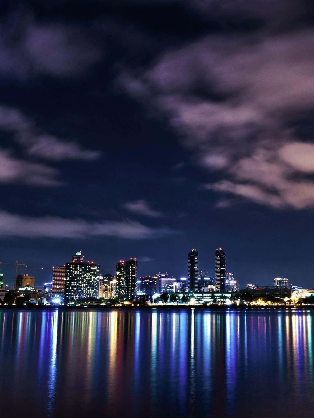 San Francisco Skyline 桌布 壁紙 — 在戲劇性的多雲天空下，寧靜的水面倒映著充滿活力的城市夜景。