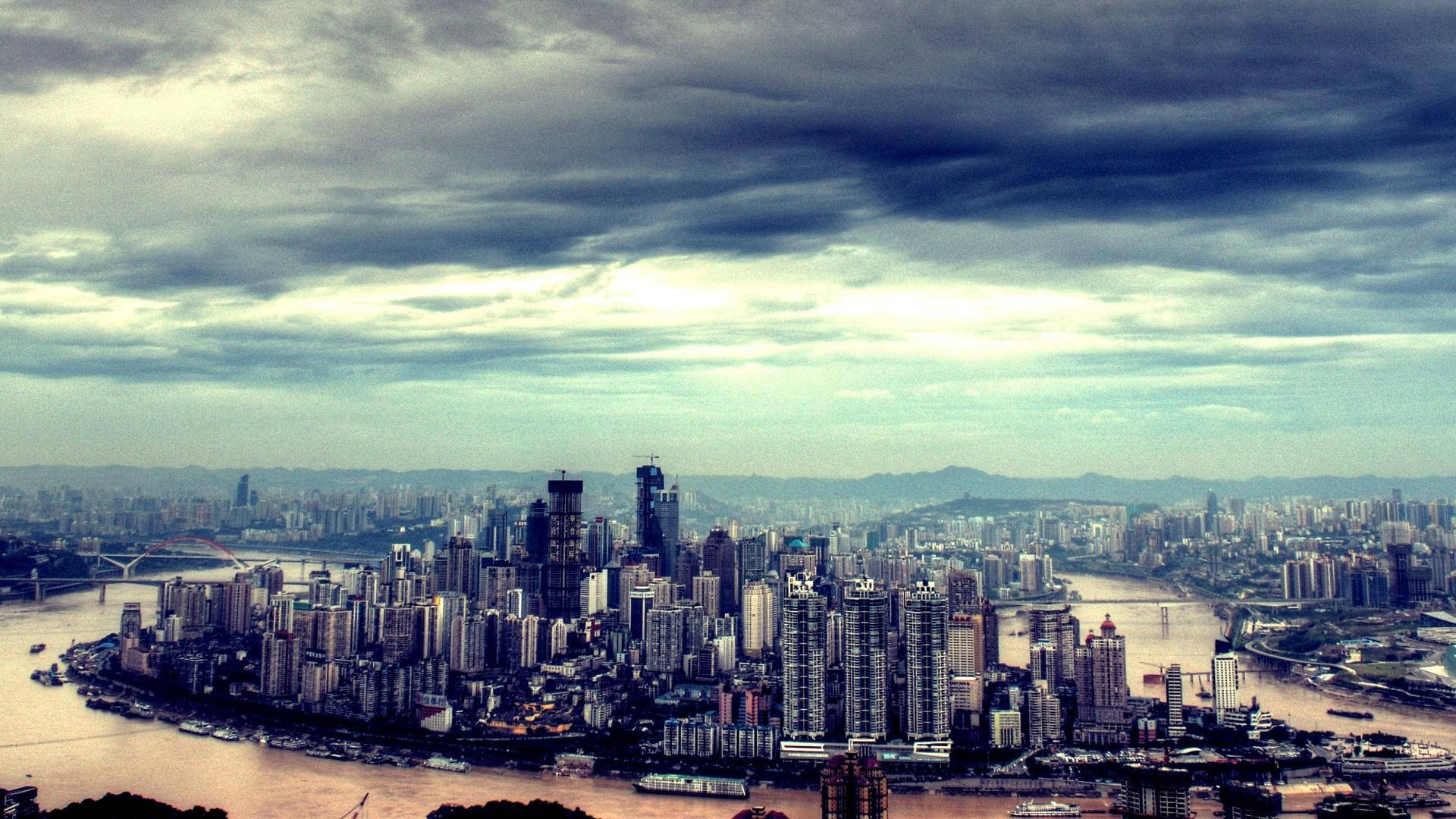 Chongqing 桌布 壁紙 — 在戲劇性的多雲天空下，廣闊的城市天際線，高聳的摩天大樓和蜿蜒的河流。