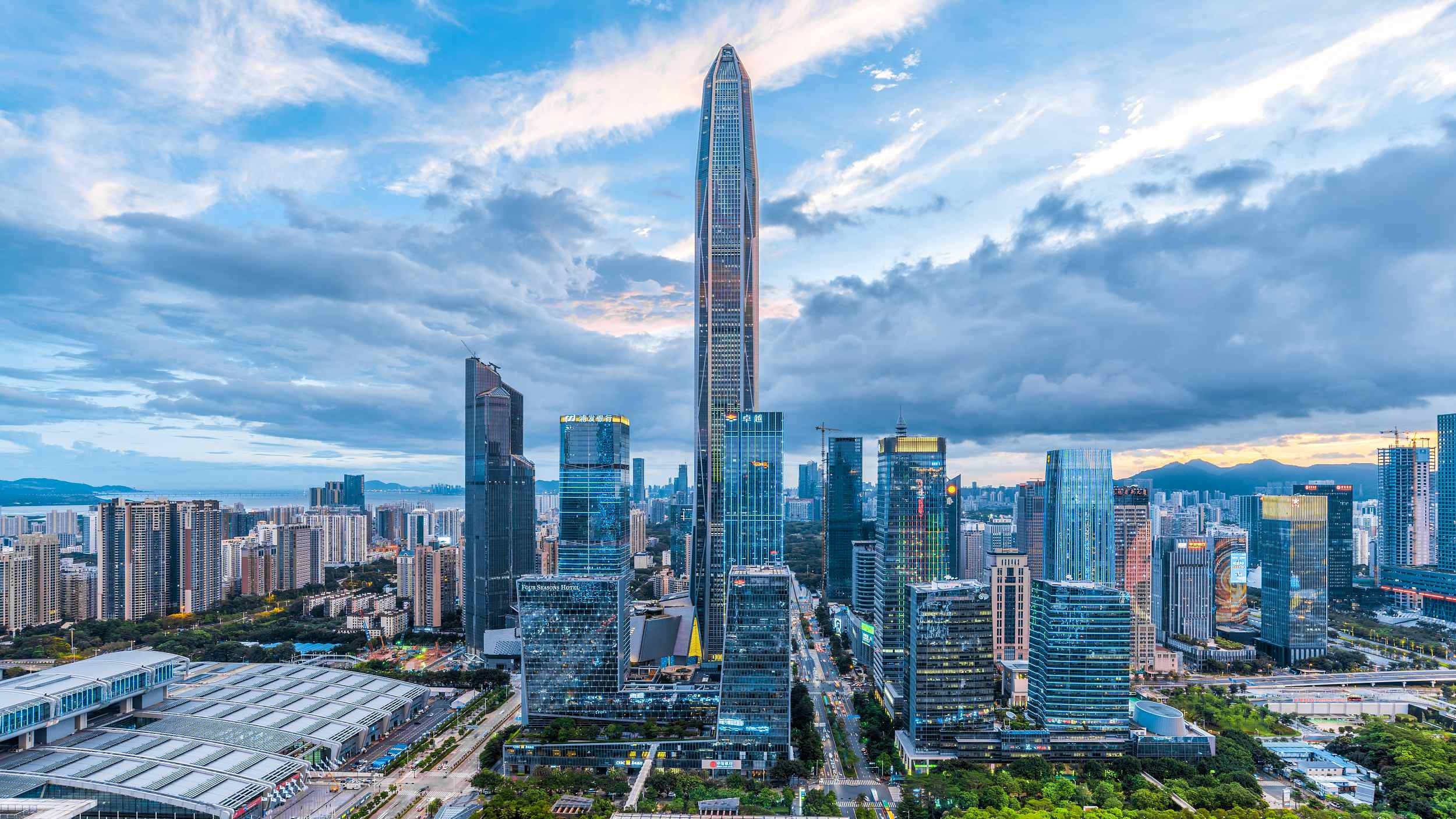 Shenzhen 桌布 壁紙 — 在戲劇性的多雲天空下，由高聳摩天大樓主導的未來城市景觀的鳥瞰圖。