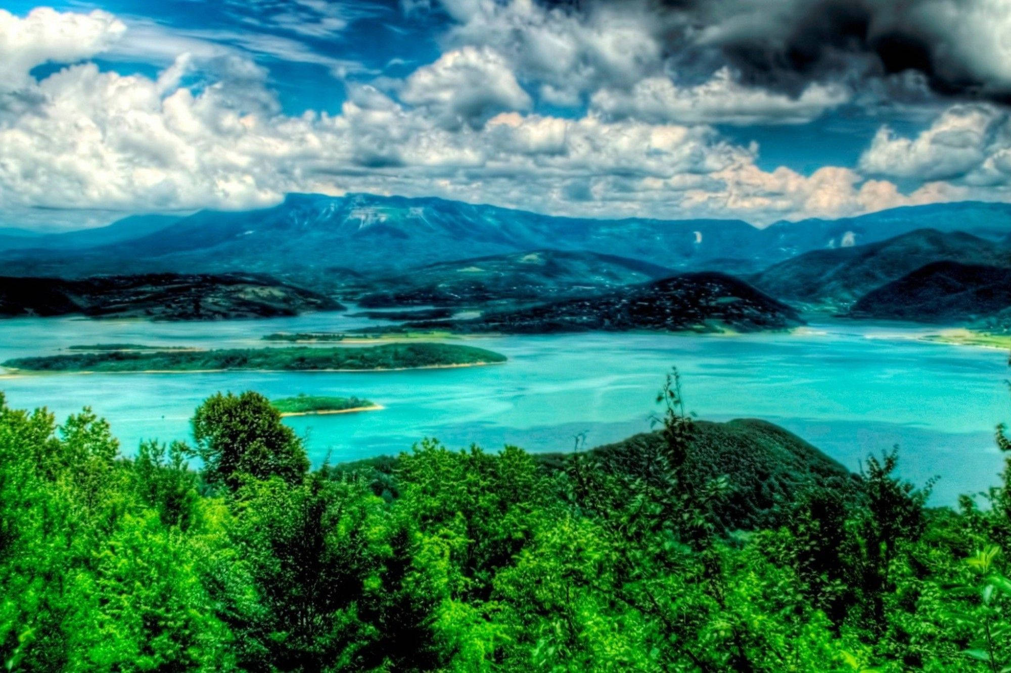 Haiti 桌布 壁紙 — 在戲劇性的多雲天空下，翠綠的森林和遠山之間鑲嵌著充滿活力的綠松石色湖泊。