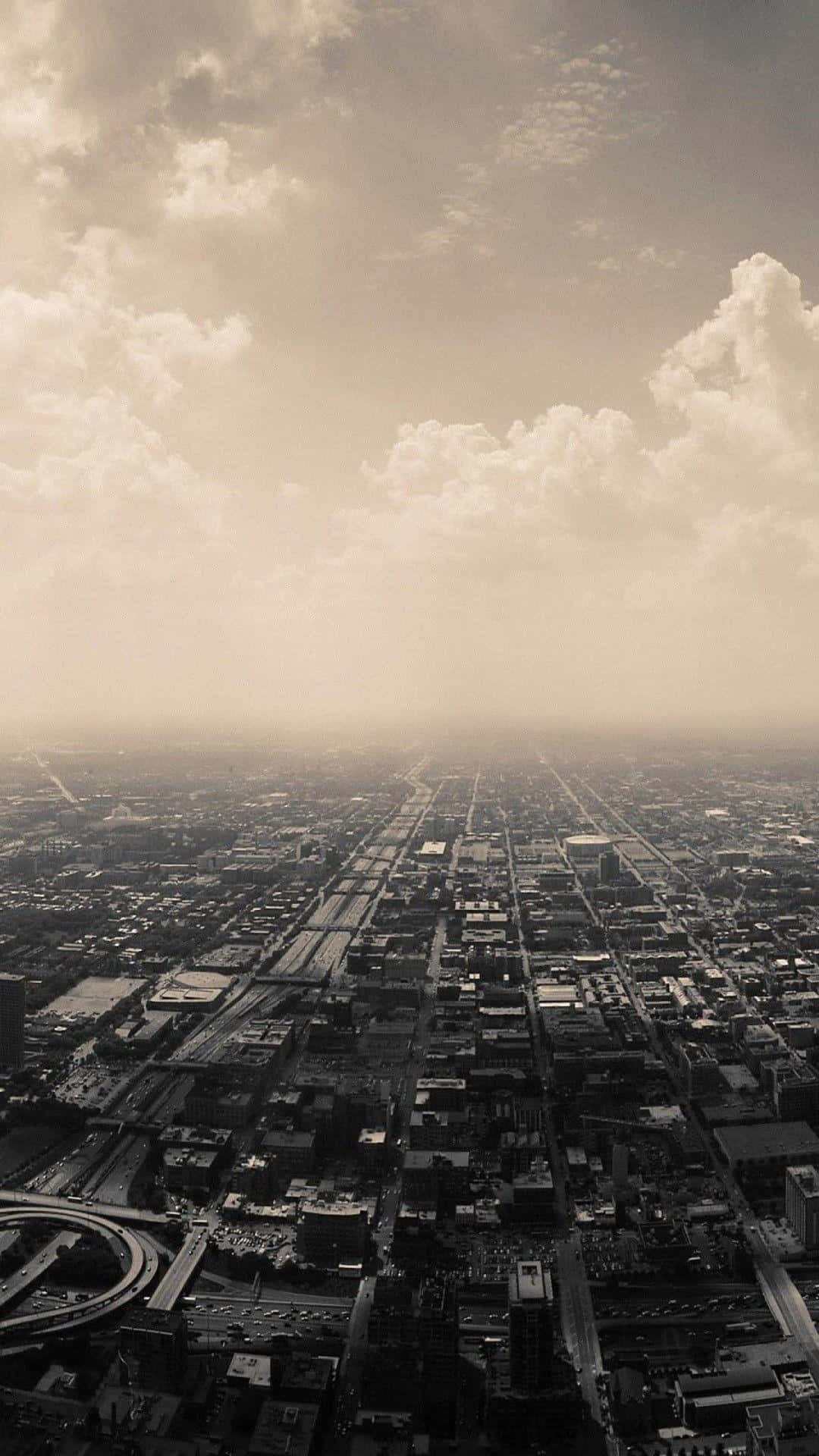 City View 桌布 壁紙 — 在戲劇性的多雲天空和薄霧下，廣闊城市網格的懷舊褐色調鳥瞰圖。