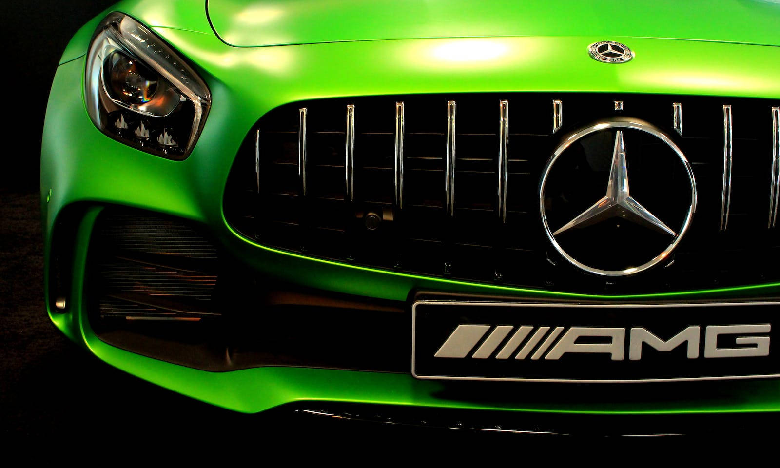 跑車 桌布 壁紙 — 在戲劇性的攝影棚燈光下，一輛充滿活力的綠色 Mercedes-AMG 汽車前格柵和標誌的特寫。