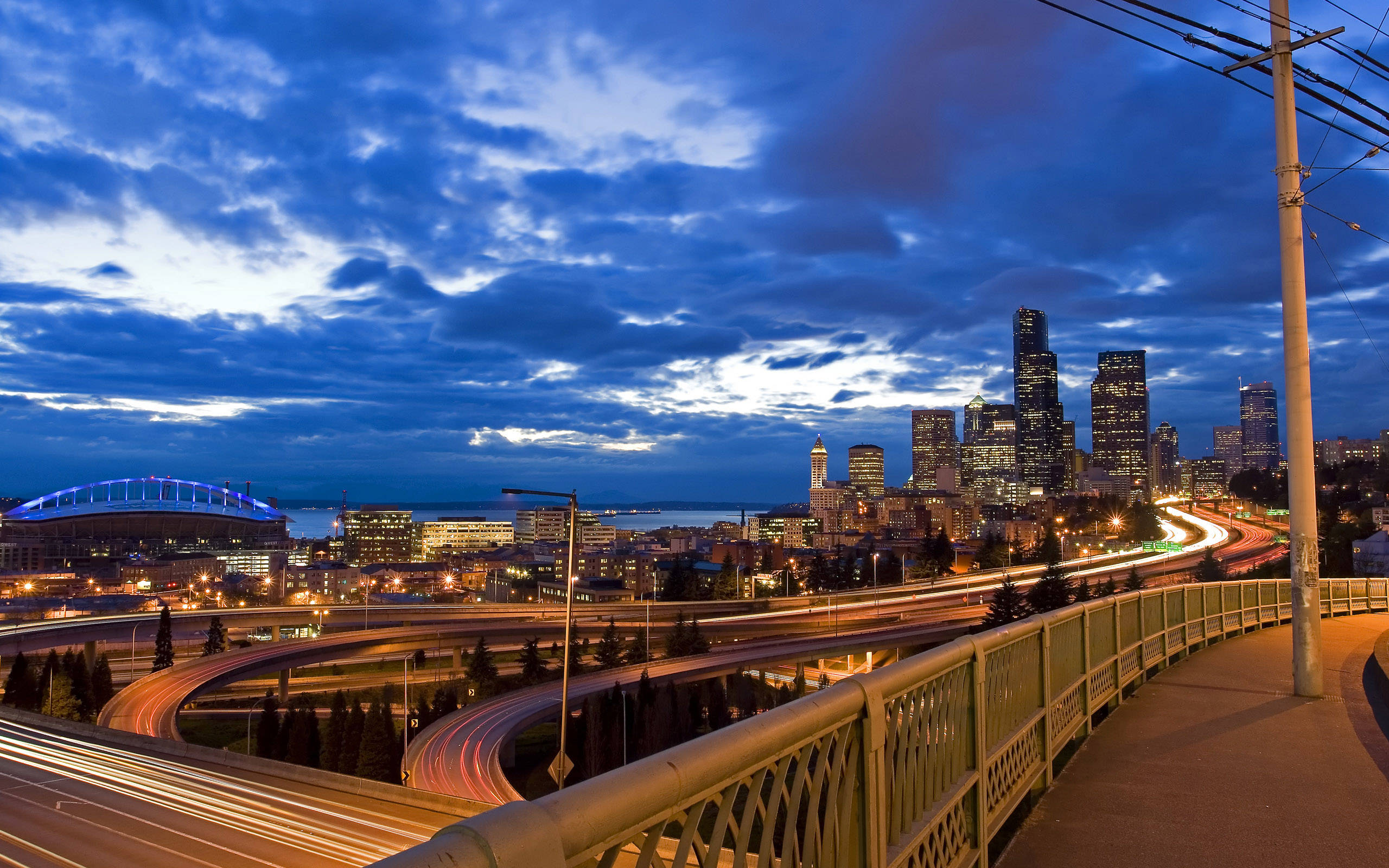 Seattle 桌布 壁紙 — 在戲劇性的藍天下，黃昏時分充滿活力的城市景觀，閃爍的摩天大樓和汽車燈光劃過天際。