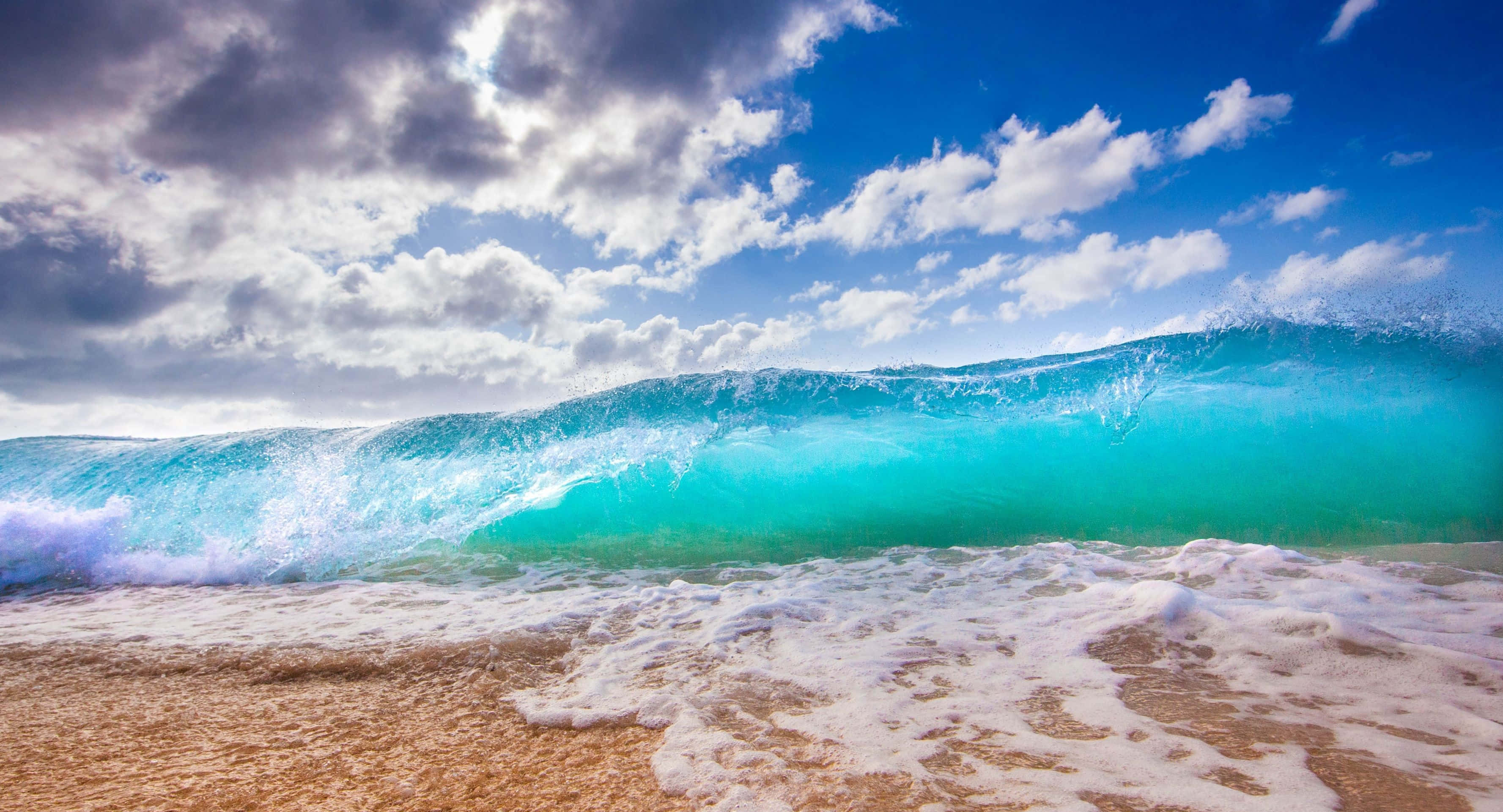 waves 桌布 壁紙 — 在戲劇性的藍天白雲下，巨大的藍綠色波浪在沙灘上翻滾。