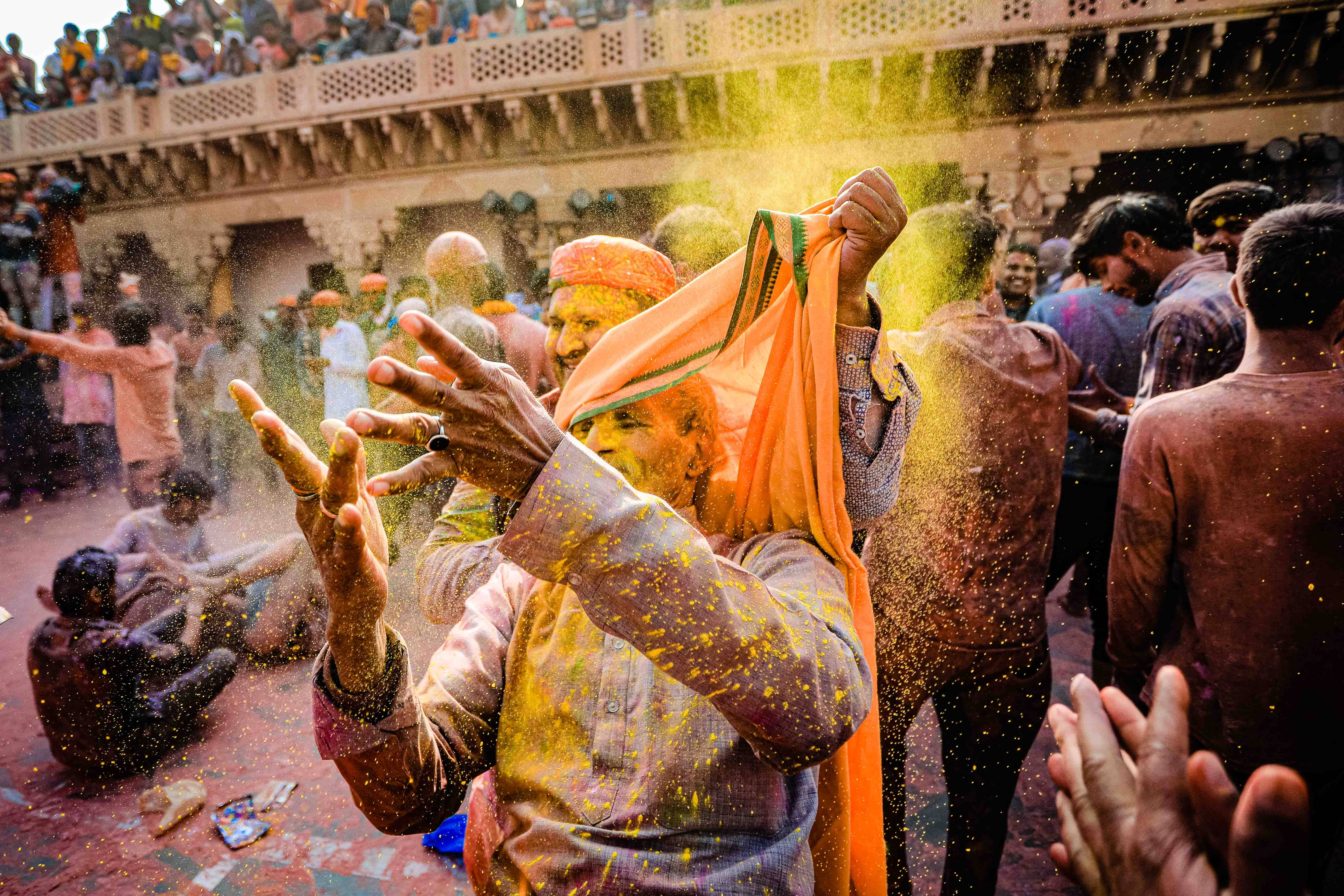 Holi 桌布 壁紙 — 在擁擠的侯麗節慶祝活動中，一名男子歡快地將鮮黃色粉末拋向空中。