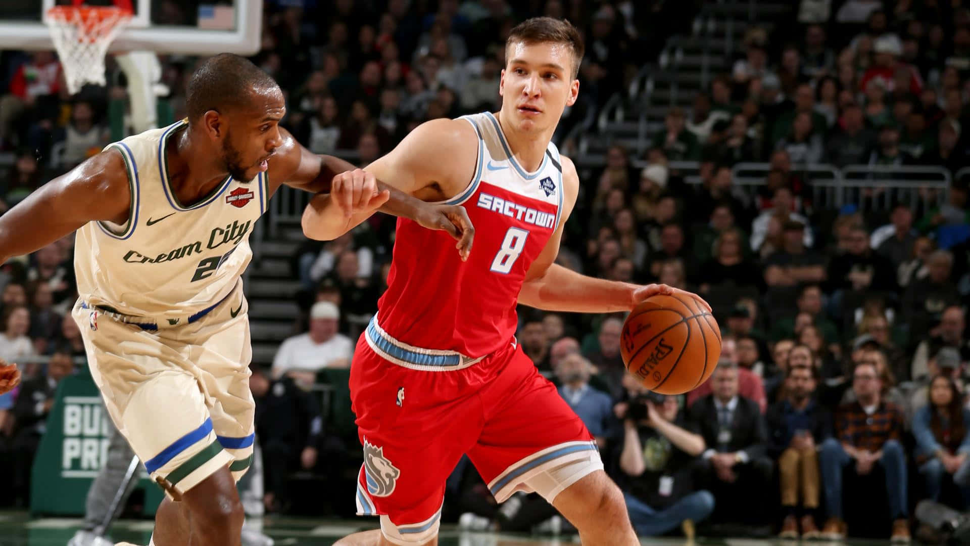 NBA 桌布 壁紙 — 在擠滿觀眾的場館比賽中，一名身穿紅色球衣的籃球運動員運球，同時被一名身穿奶油色球衣的防守球員緊密防守。