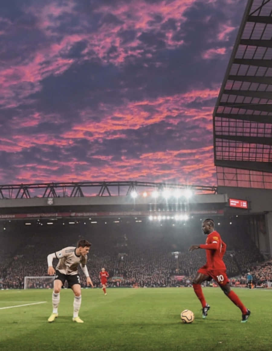 Soccer Aesthetic 桌布 壁紙 — 在擠滿觀眾的體育場內，兩名足球運動員在戲劇性的粉紅和紫色日落天空下爭奪控球權。
