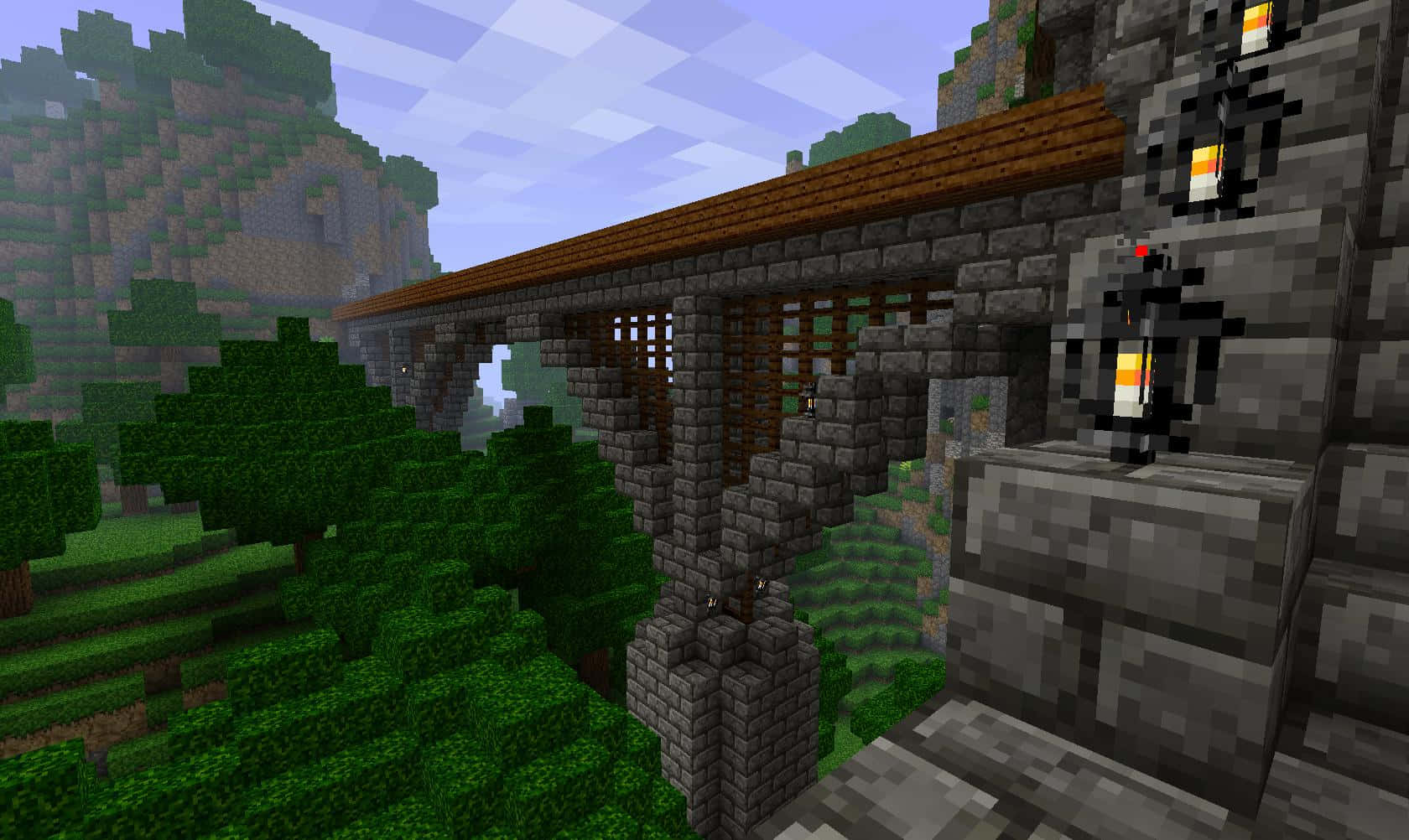 Minecraft Bridges 桌布 壁紙 — 在方塊天空下，Minecraft 景觀中一座像素化的石橋帶有木頂橫跨翠綠的山谷。