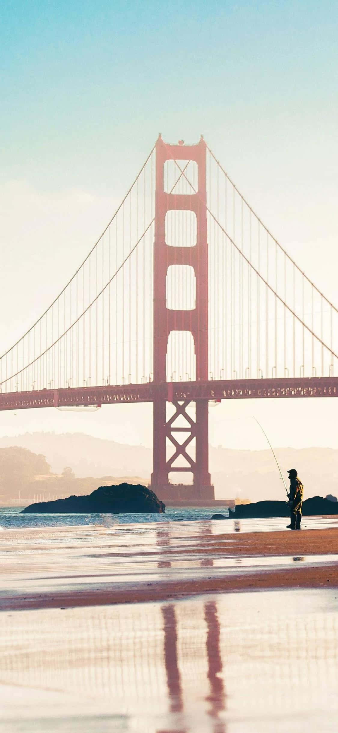bridge 桌布 壁紙 — 在日出時分，一位孤獨的漁夫在霧氣瀰漫的海灘上，在雄偉的紅色金門大橋下拋線。