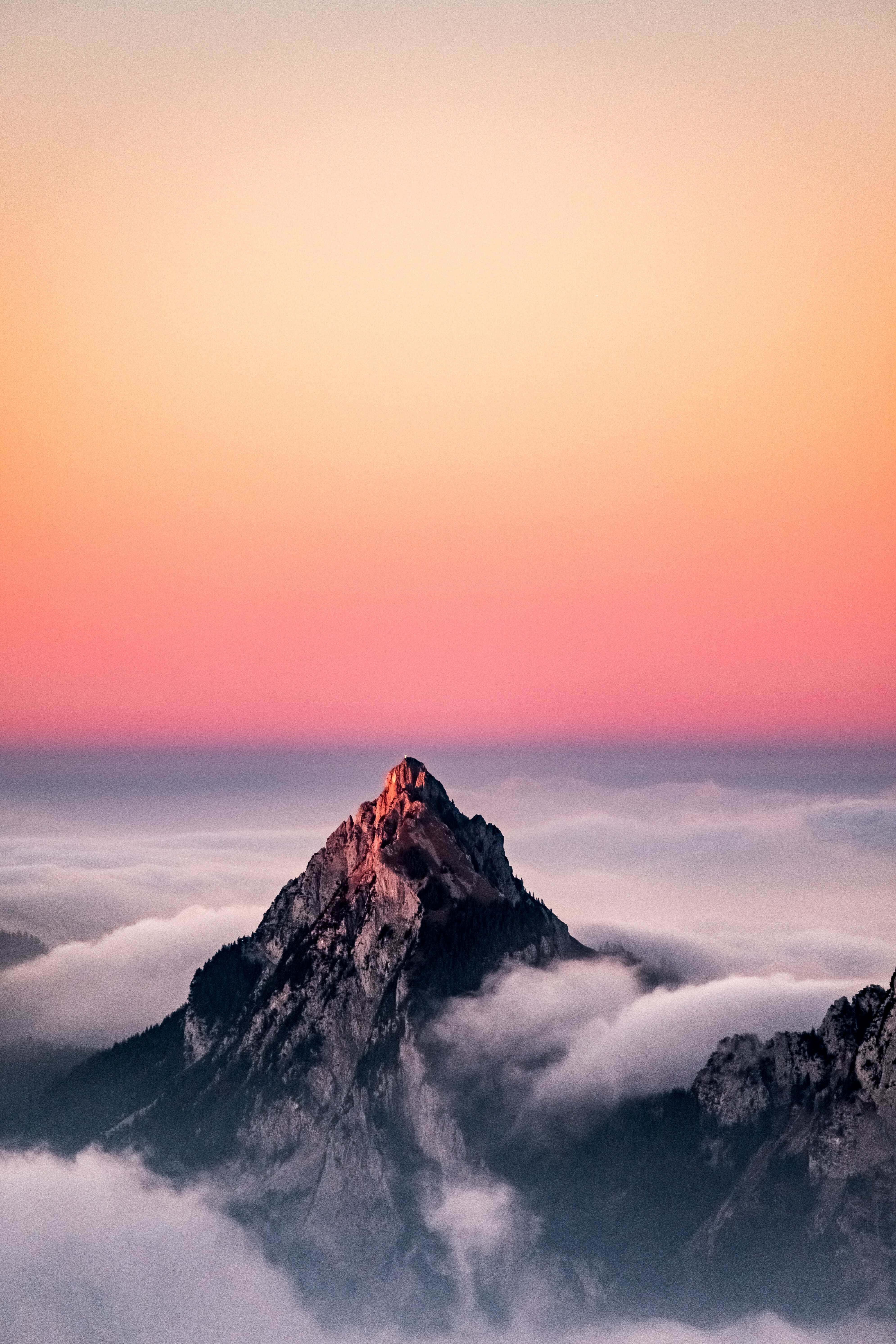 山景 桌布 壁紙 — 在日出時分，一個鋸齒狀的山峰在粉紅色、橙色和紫色的漸變天空下刺穿雲海。