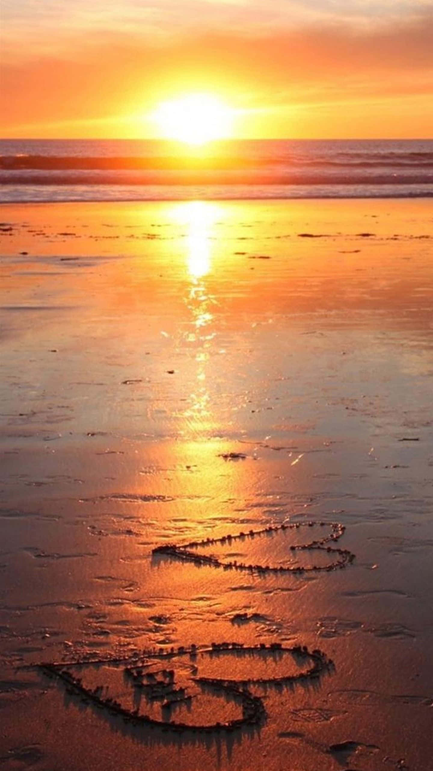 Beach Love 桌布 壁紙 — 在日落時分，金色光芒映照海洋，濕沙上畫有一顆心和一支箭。