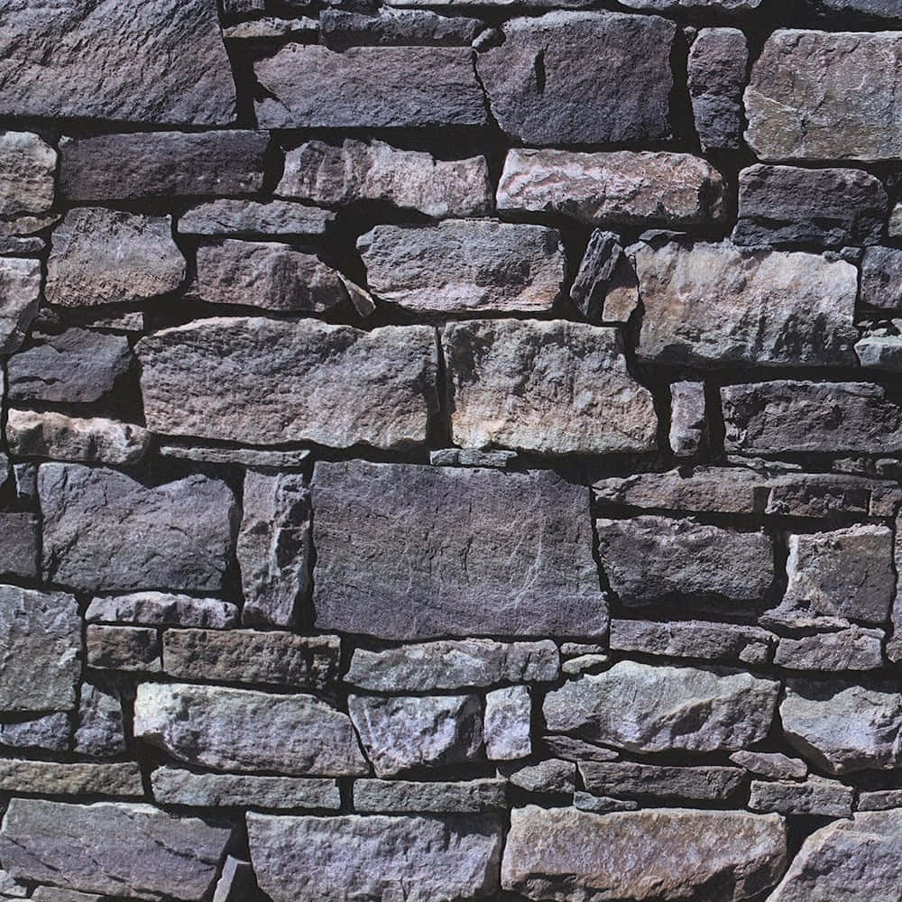 Brick Wall 桌布 壁紙 — 在明亮日光下，一個粗糙石牆的特寫，帶有不同灰色和棕色色調以及粗糙紋理。