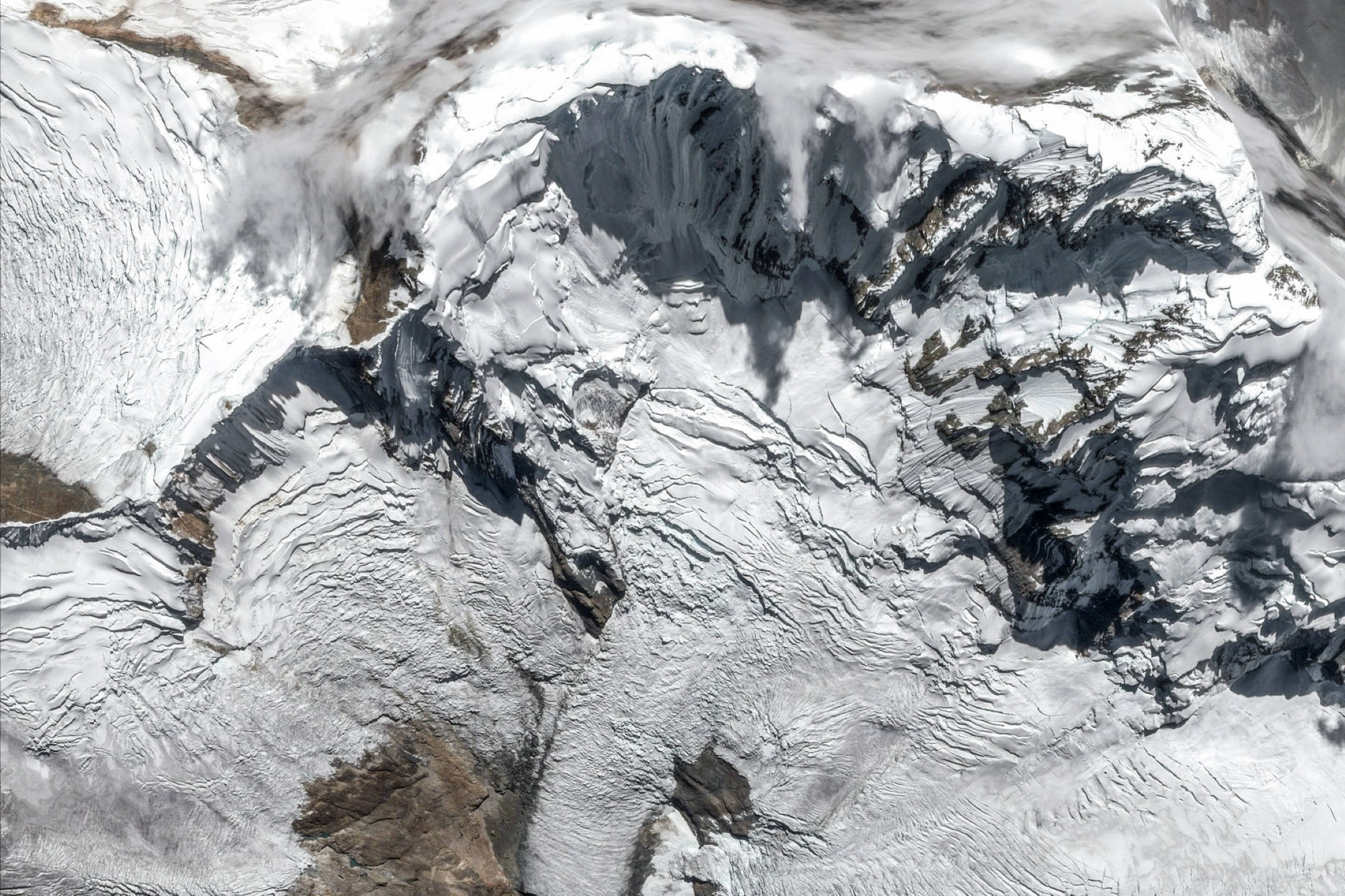 Google 地球 桌布 壁紙 — 在明亮日光下，崎嶇積雪山脈的鳥瞰圖，帶有深裂縫和岩石露頭。