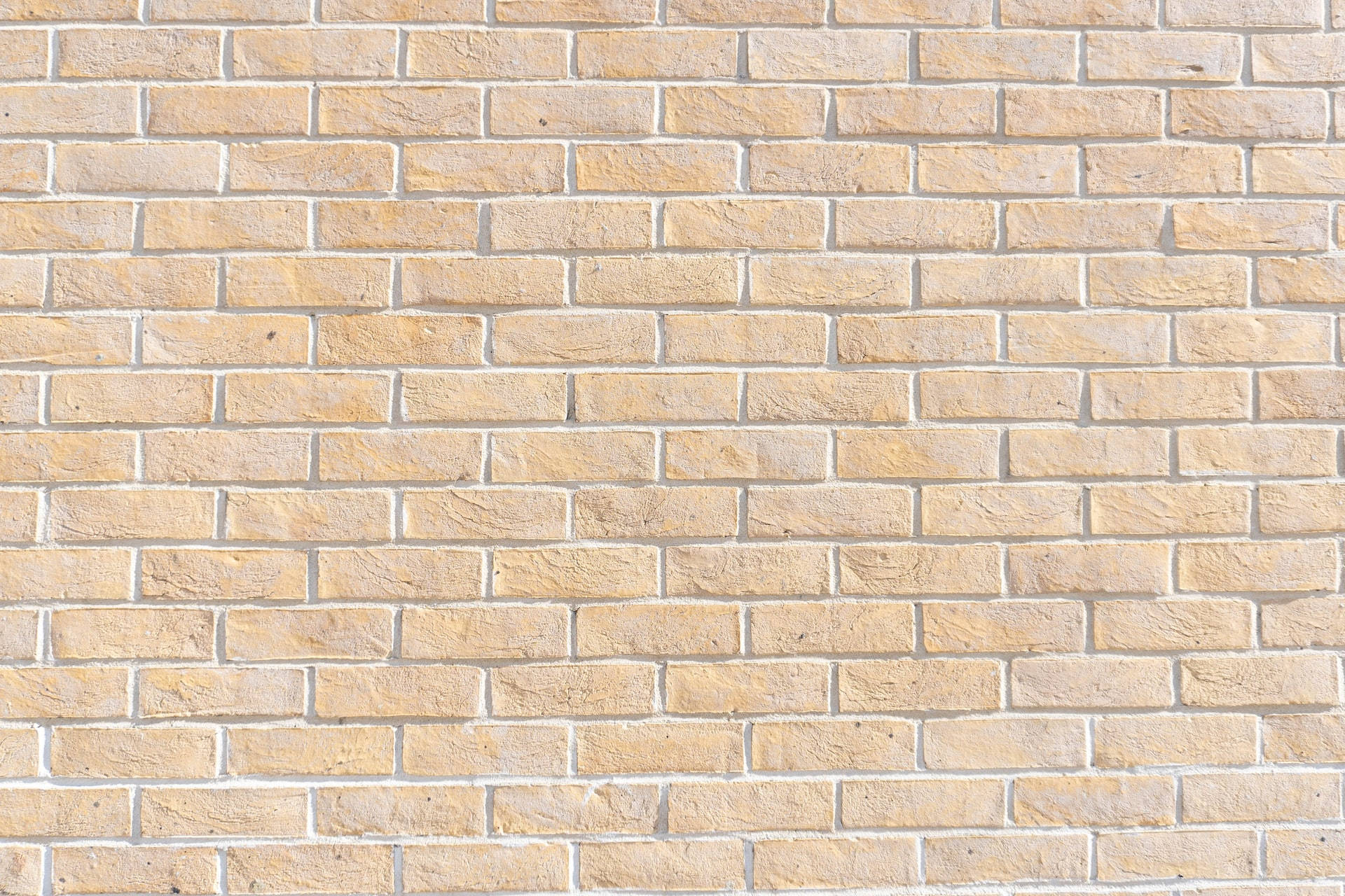 Brick 桌布 壁紙 — 在明亮日光下，帶有紋理砂漿線條和天然石材般磚塊的米色磚牆特寫。
