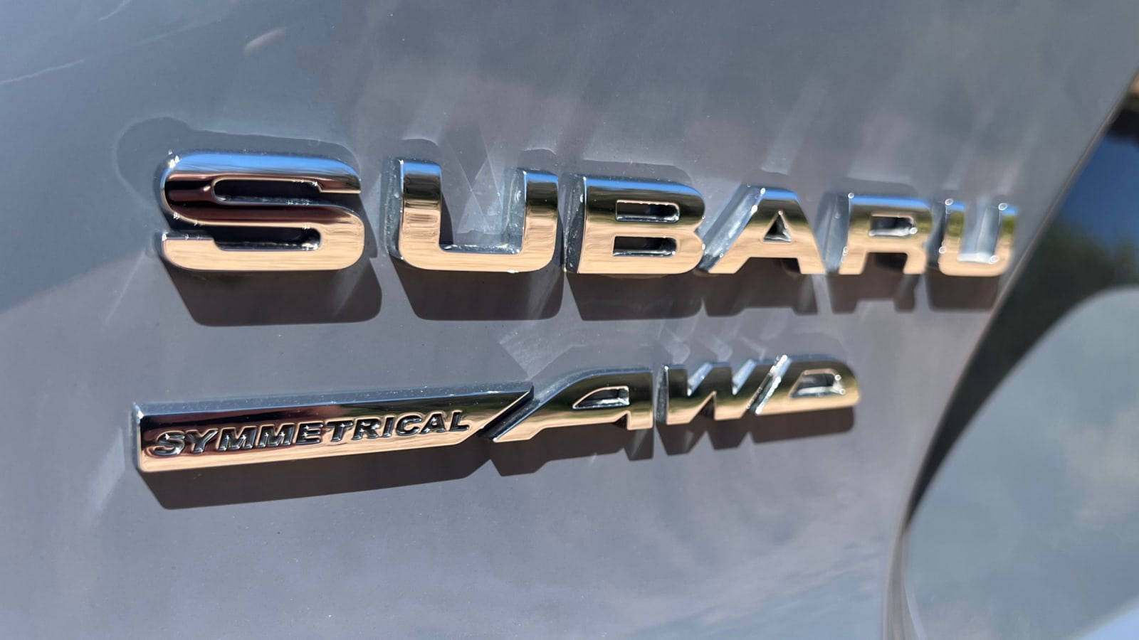 速霸陸標誌 桌布 壁紙 — 在明亮日光下，時尚灰色引擎蓋上的鍍鉻 Subaru Symmetrical AWD 徽章特寫。