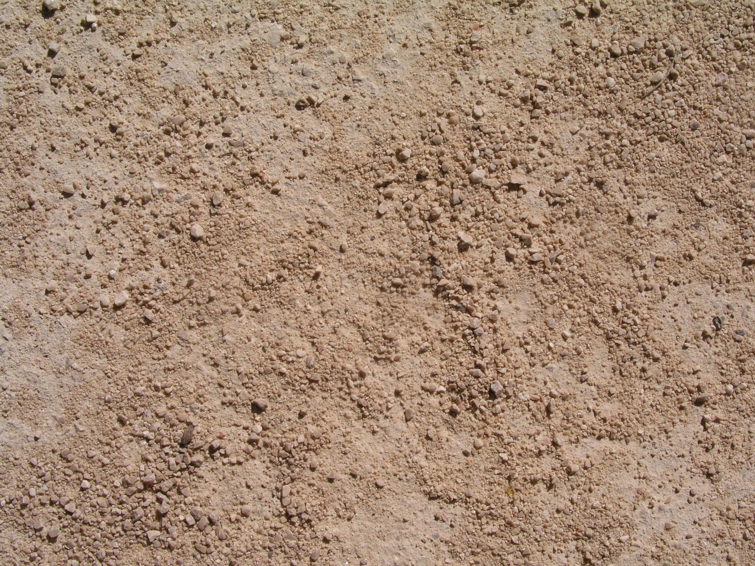 Dirt 桌布 壁紙 — 在明亮日光下，粗糙沙質地形上散落著小卵石的近距離特寫。