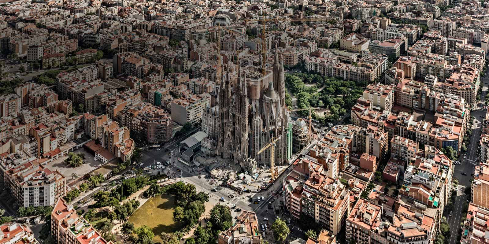 Barcelona 桌布 壁紙 — 在明亮日光下，聖家堂大教堂在密集的巴塞隆納屋頂上崛起的航拍景觀。