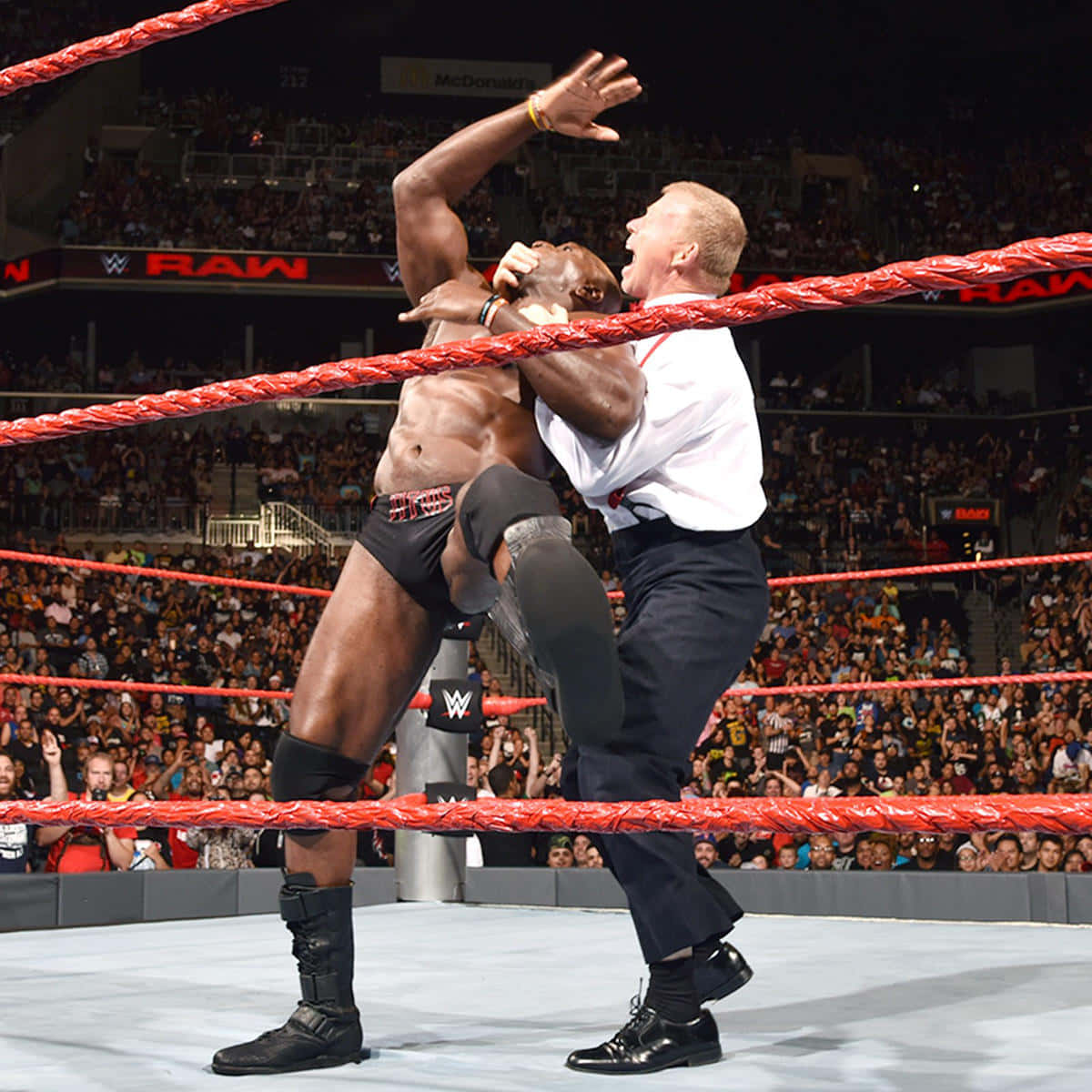 WWE 桌布 壁紙 — 在明亮的場館燈光下，一名摔角手在WWE擂台上戲劇性地舉起裁判。