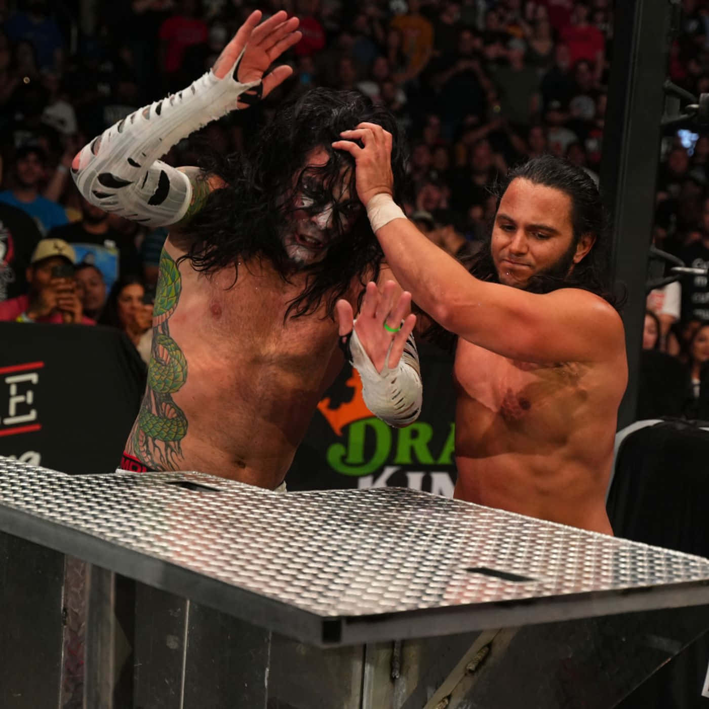 WWE 桌布 壁紙 — 在明亮的場館燈光下，兩名摔角手在一場混亂的職業摔角比賽中，在一張鋼桌上激烈纏鬥。