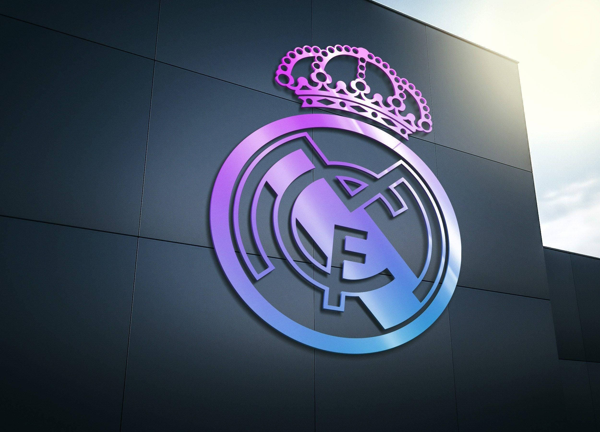 Real Madrid 4K 桌布 壁紙 — 在明亮的日光下，一個發光的紫色和藍色皇家馬德里徽章（帶有皇冠）位於深色現代建築外牆上。