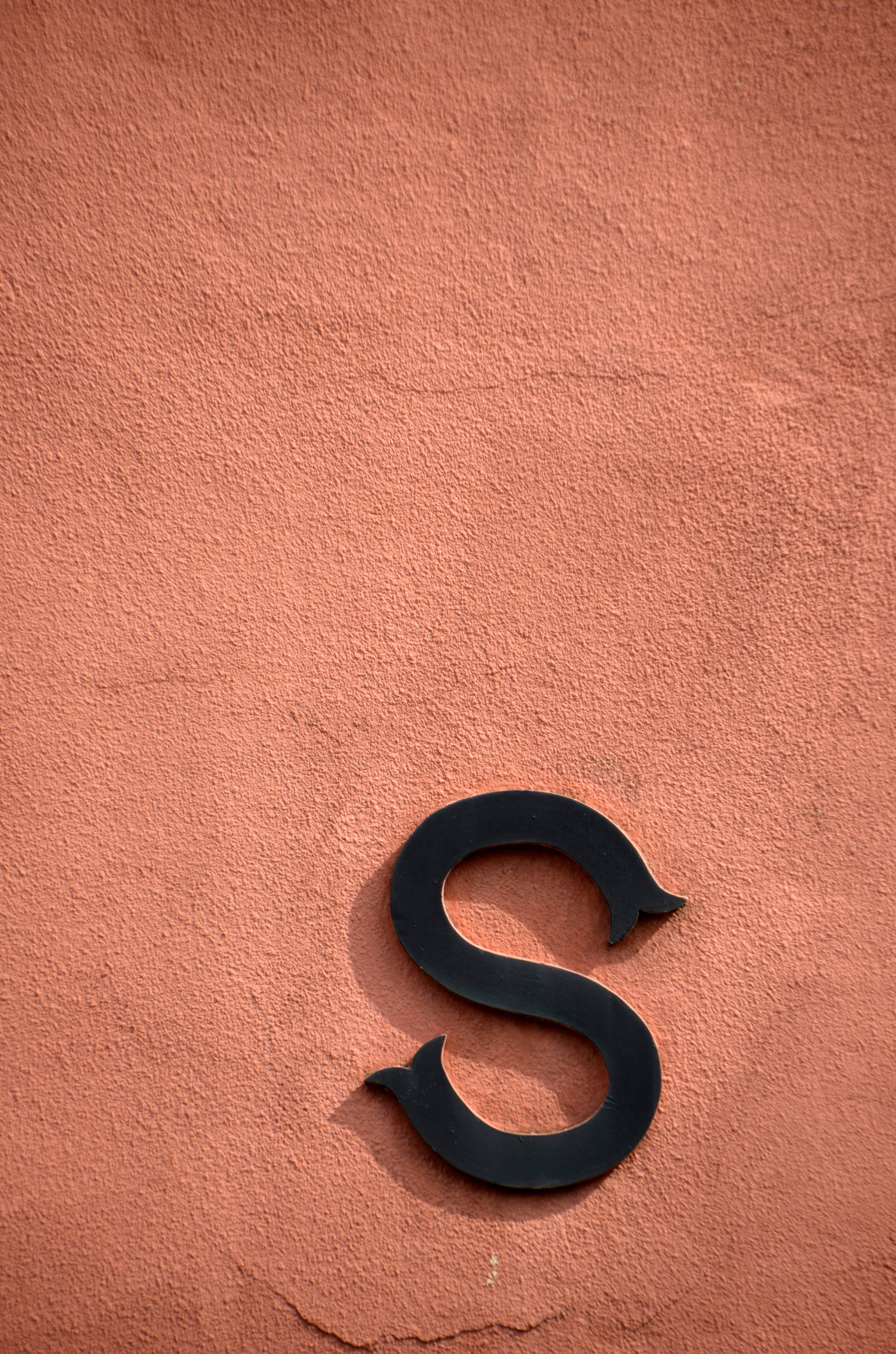 S Alphabet 桌布 壁紙 — 在明亮的日光下，一個粗體黑色字母S安裝在有紋理的赤陶牆上。