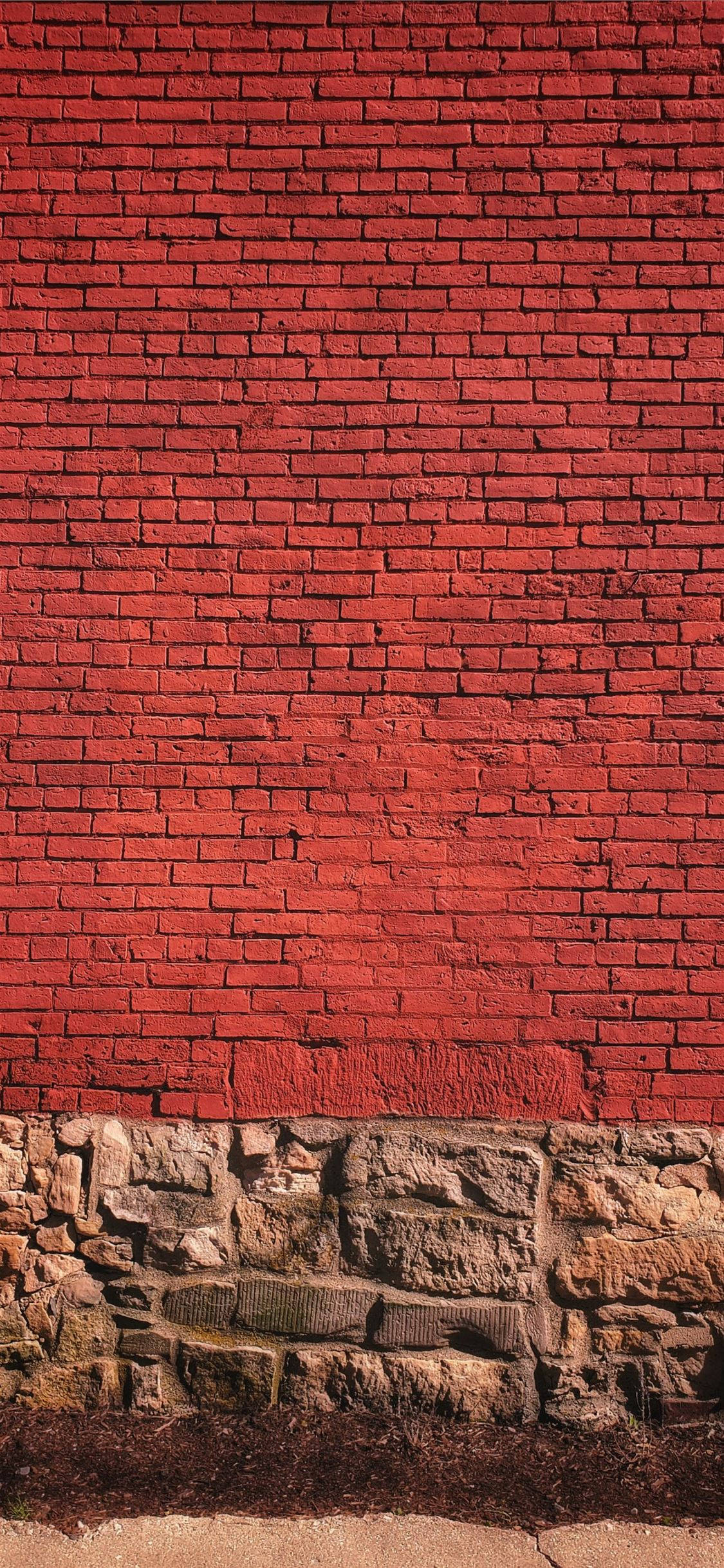 Brick 桌布 壁紙 — 在明亮的日光下，一座帶粗糙石地基的高紅磚牆。