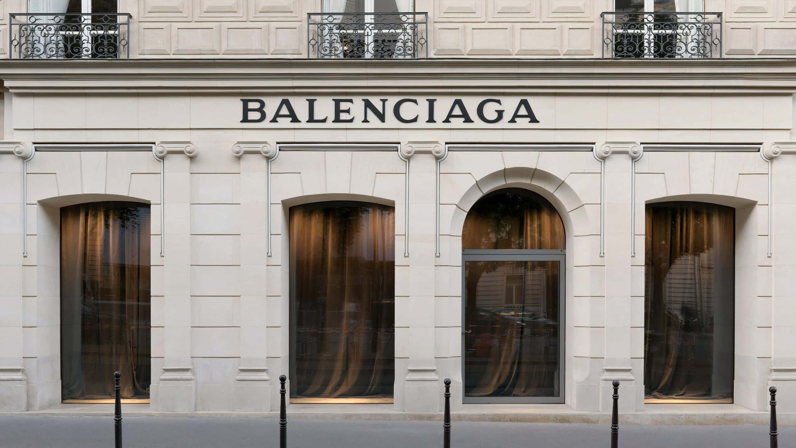 巴黎世家 桌布 壁紙 — 在明亮的日光下，純白色的 Balenciaga 精品店外牆，配有拱形窗戶和優雅的鐵藝陽台。